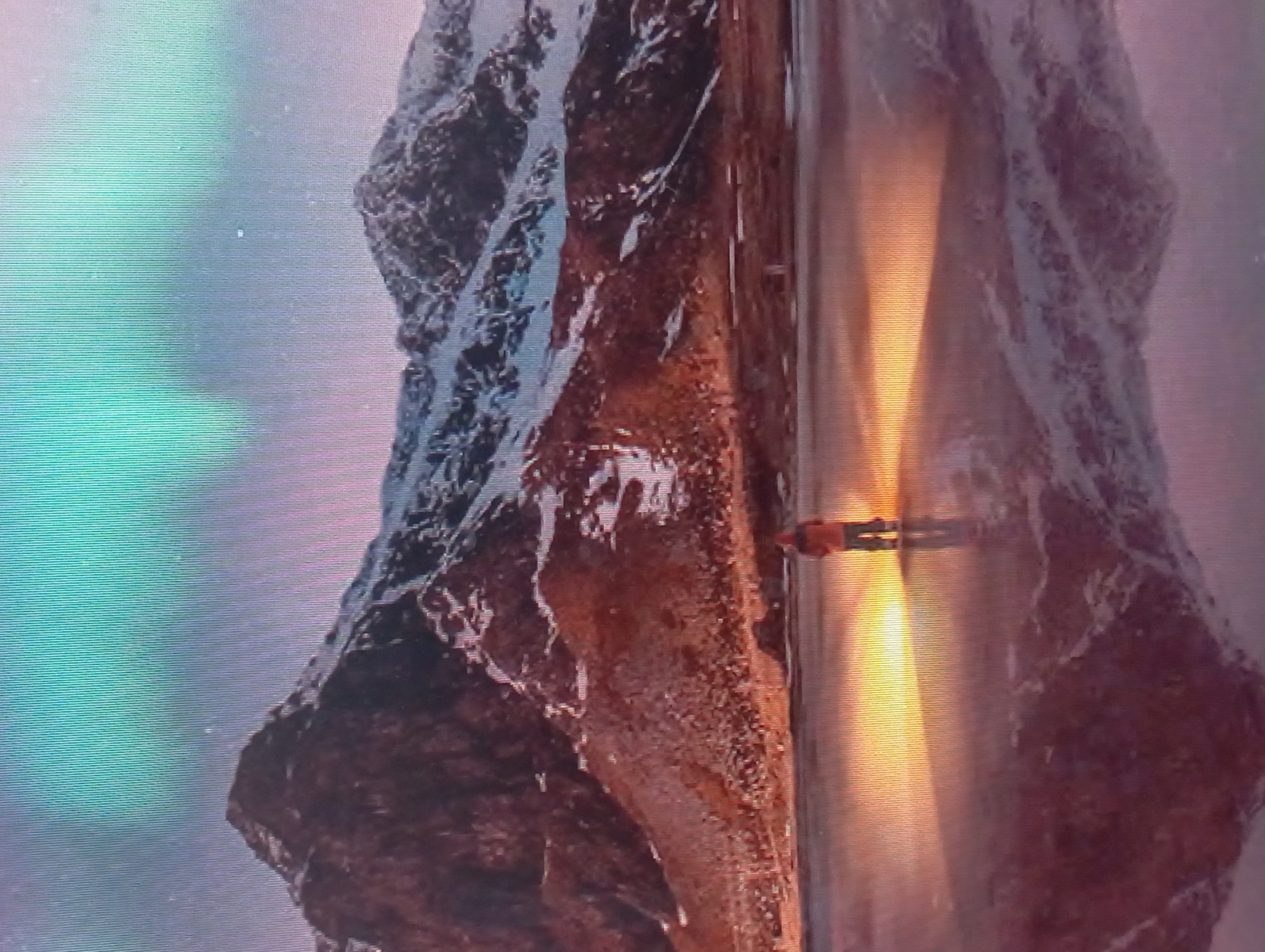 The image depicts a person walking on a brightly lit surface, likely a pathway or platform. The person's figure is small relative to the surroundings, suggesting a vast environment. On either side of the pathway are large, rugged rock formations. The image appears to be shot from a slightly elevated perspective. The setting is not discernable as Karaganda, Kazakhstan without further information.