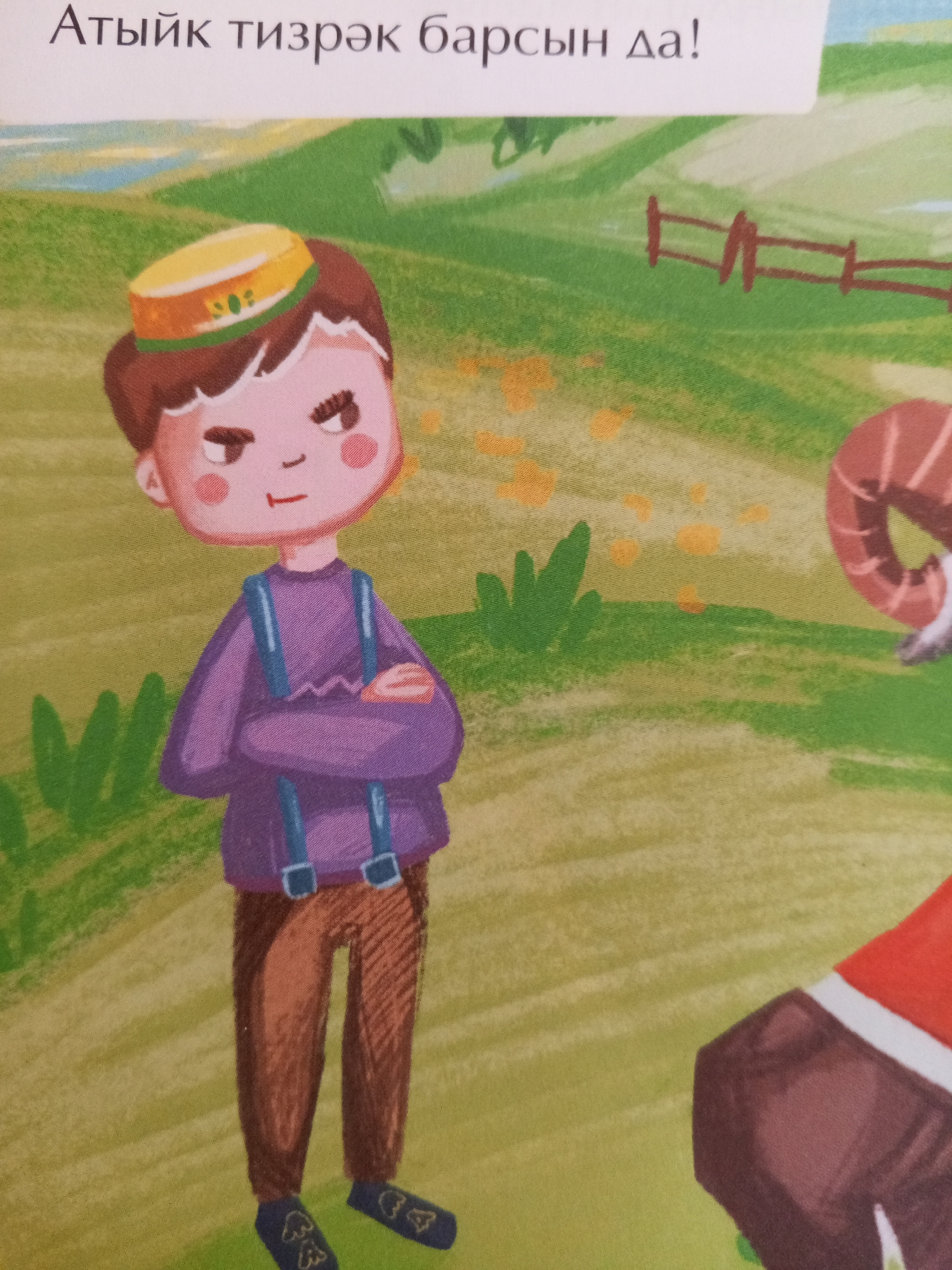 The image is a close-up, eye-level shot of a children's book illustration. The foreground features a cartoon boy with brown hair, a yellow hat with a green band and a small emblem, rosy cheeks, and an annoyed expression. He is wearing a purple long-sleeved shirt with blue suspenders and brown pants, with his arms crossed. His feet are in dark blue shoes with white symbols. To the right, a portion of a brown and white sheep or ram is visible, wearing a red garment. The background depicts a grassy, hilly landscape with a simple wooden fence. The scene is brightly colored and stylized, typical of children's book art. The text at the top of the image is in Cyrillic script. The image is a digital artwork, likely part of a larger narrative or educational material for children. There is no visible indication of the city of Chistopol, Russia within the image itself; this information is external to the visual content.