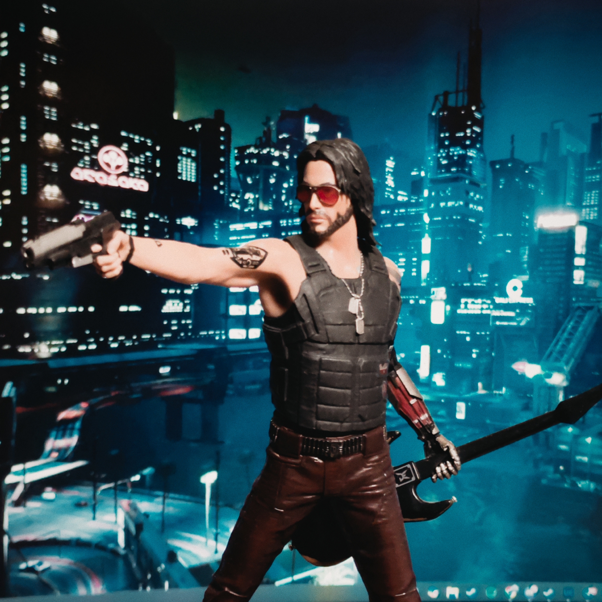 A figure, resembling a character from the Cyberpunk 2077 video game, is presented against a backdrop of a futuristic cityscape at night. The figure wears sunglasses, a black vest, brown pants, and a necklace with dog tags. A pistol is held in the figure's right hand, while a guitar is in the left. The backdrop reveals neon-lit skyscrapers. The Arasaka Corporation logo is visible on a building. The city of Budva, Montenegro, is not present in the image.