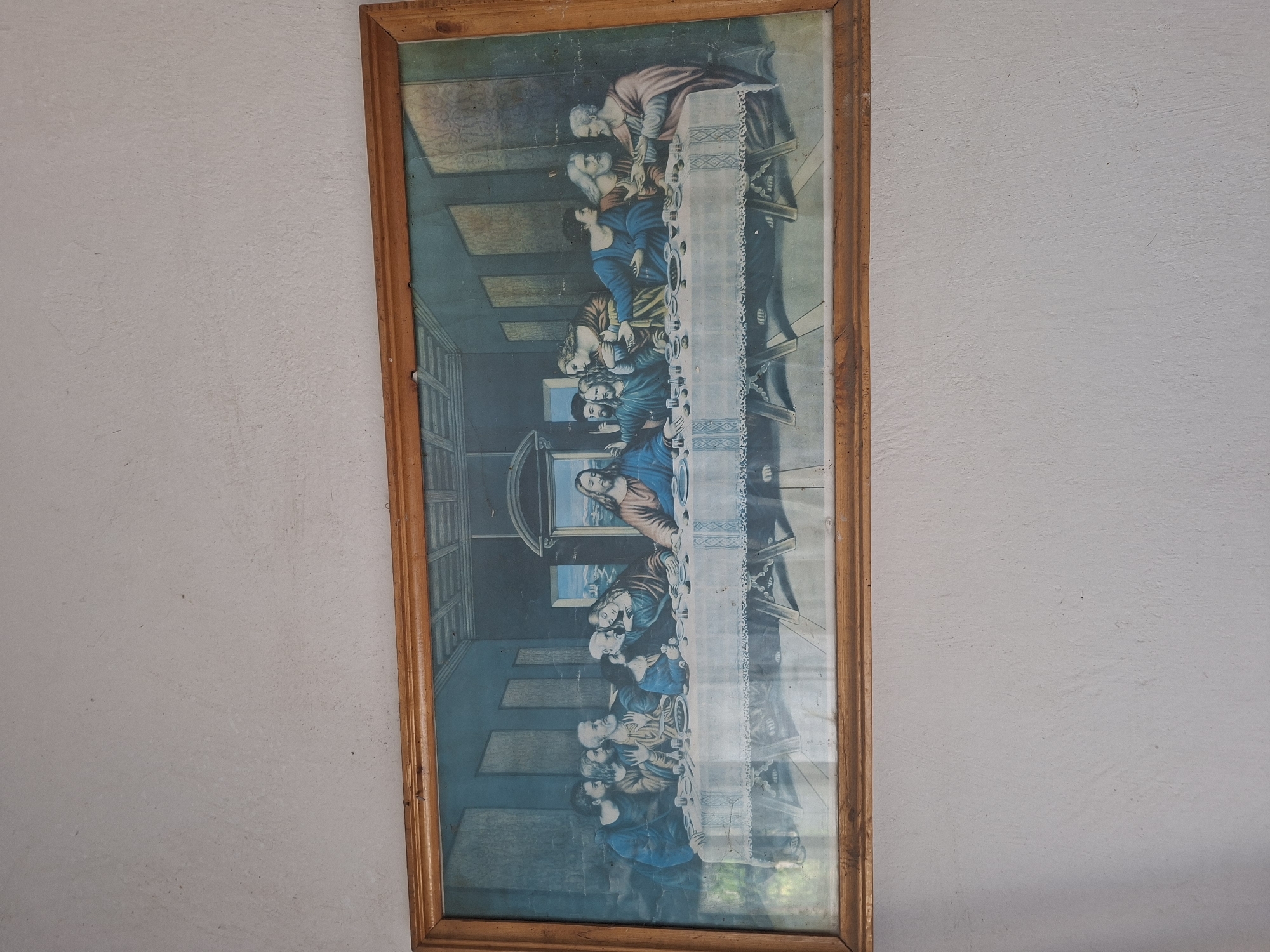 A framed print of Leonardo da Vinci's "The Last Supper" hangs vertically on a light-colored wall. The frame is made of wood, with a clear protective covering over the print. The wall itself appears to be textured and painted a light gray or off-white color. No people are visible in the image. The image suggests an indoor location. Without additional context, the specific location in Pokrovan, Bulgaria cannot be determined from the visual information provided.