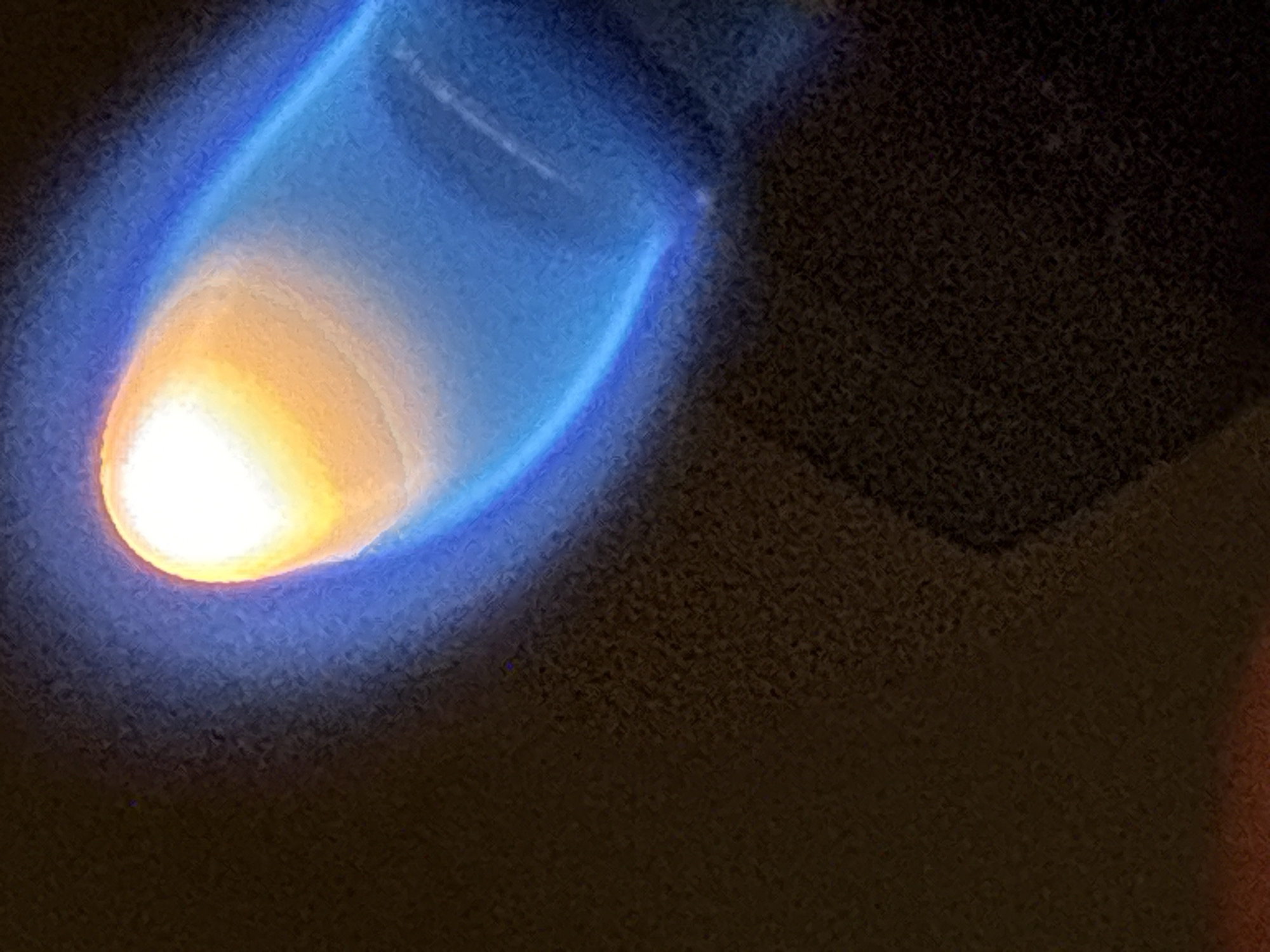 The image shows a close-up, abstract view of a flame. The flame is predominantly blue with a bright yellow-orange core at the tip. The background is dark and textured, suggesting a dimly lit environment. There are no discernible elements of the city of Plovdiv, Bulgaria, present in the image.