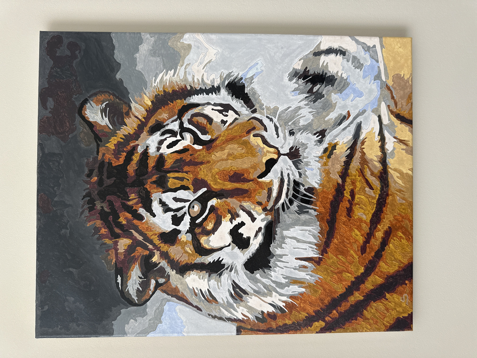 The image shows a square painting of a tiger's head, viewed at a slight angle. The painting is rendered in a blocky, somewhat stylized manner, with visible brushstrokes and distinct color areas. The tiger's fur is depicted in shades of orange, brown, black, and white, while the background varies from dark gray on the left to lighter gray and beige on the right. The painting is hanging on a light beige or off-white wall. There is no evidence to suggest this image is related to the city of Oryol, Russia.