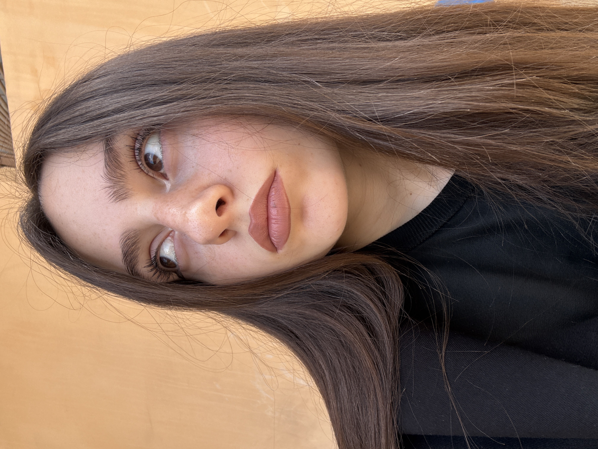 A young woman with light skin, brown hair, and brown eyes is shown in a close-up portrait. She is wearing a dark-colored shirt. The background appears to be a light-colored wooden surface. No information indicates that the location is Yerevan, Armenia.