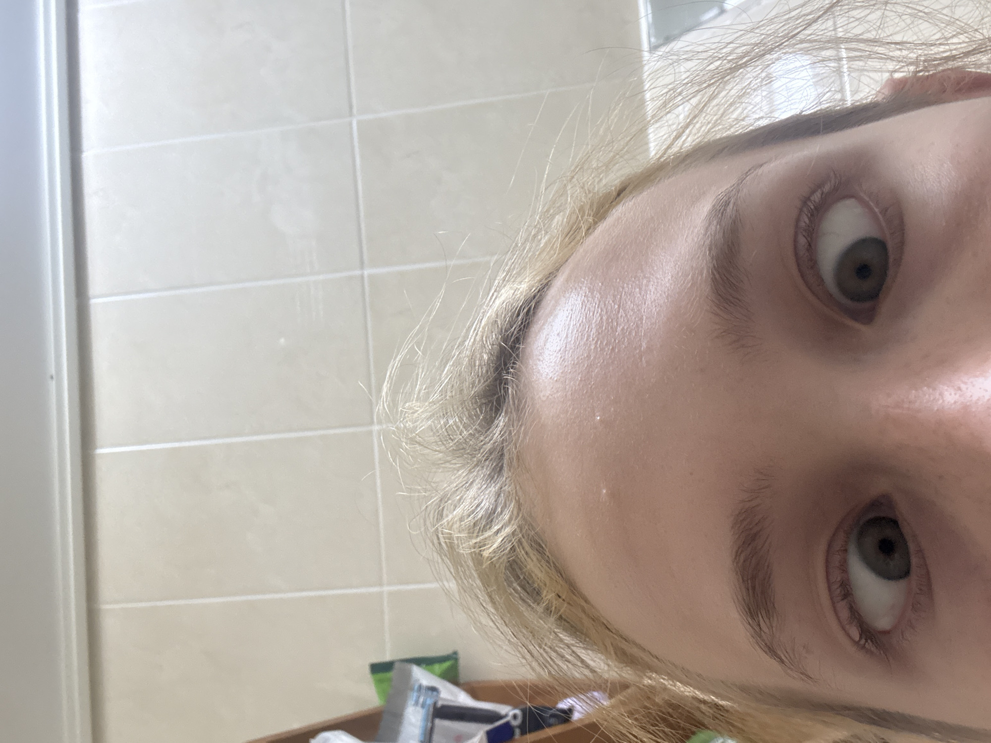 The image shows a close-up, low-angle shot of a young person's face, focusing on their forehead and eyes, with their eyes crossed. The background consists of beige-colored tiles, suggesting an indoor environment, possibly a bathroom. Some blonde hair is visible, framing the face. There are no identifiable landmarks or contextual elements that would indicate the location as Gwangju, South Korea.