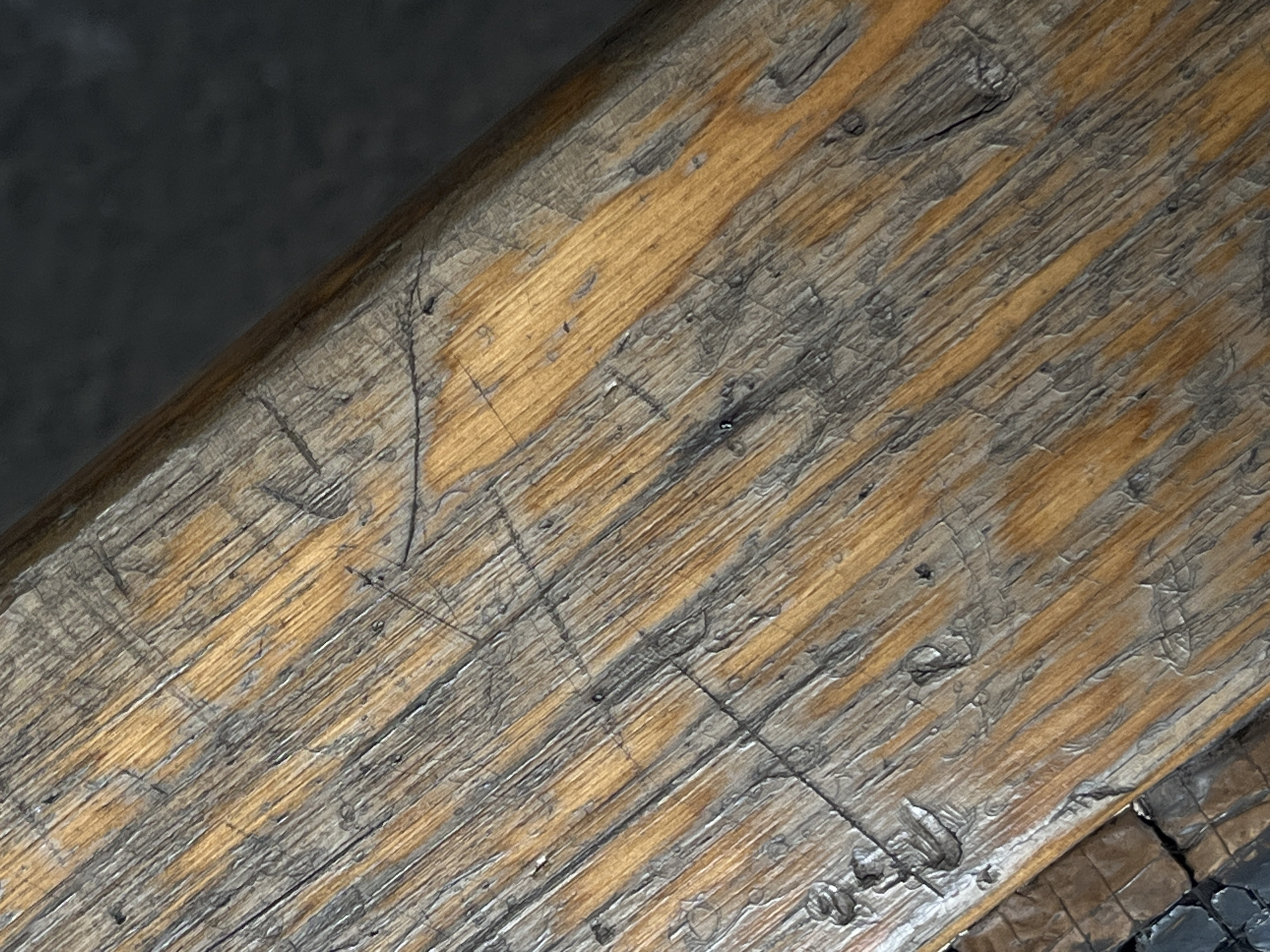 This media file shows a close-up, angled view of a weathered wooden surface, likely a plank or beam. The wood has a prominent grain pattern, with alternating streaks of light golden brown and darker greyish-brown, suggesting age and exposure. Numerous fine scratches and deeper gouges crisscross the surface, indicating wear and tear. Some areas appear smoother, while others have a rougher texture with small pits and raised fibers.
The background is dark and out of focus, creating a strong contrast with the textured wood in the foreground. The lighting suggests it might be indoor lighting or overcast daylight, as there are no harsh shadows. The overall impression is one of ruggedness and a rustic aesthetic. There is no visible text or any indication of people, animals, or specific objects beyond the wooden surface itself. The location context of Kyiv, Ukraine, does not provide any direct visual cues within the image itself.