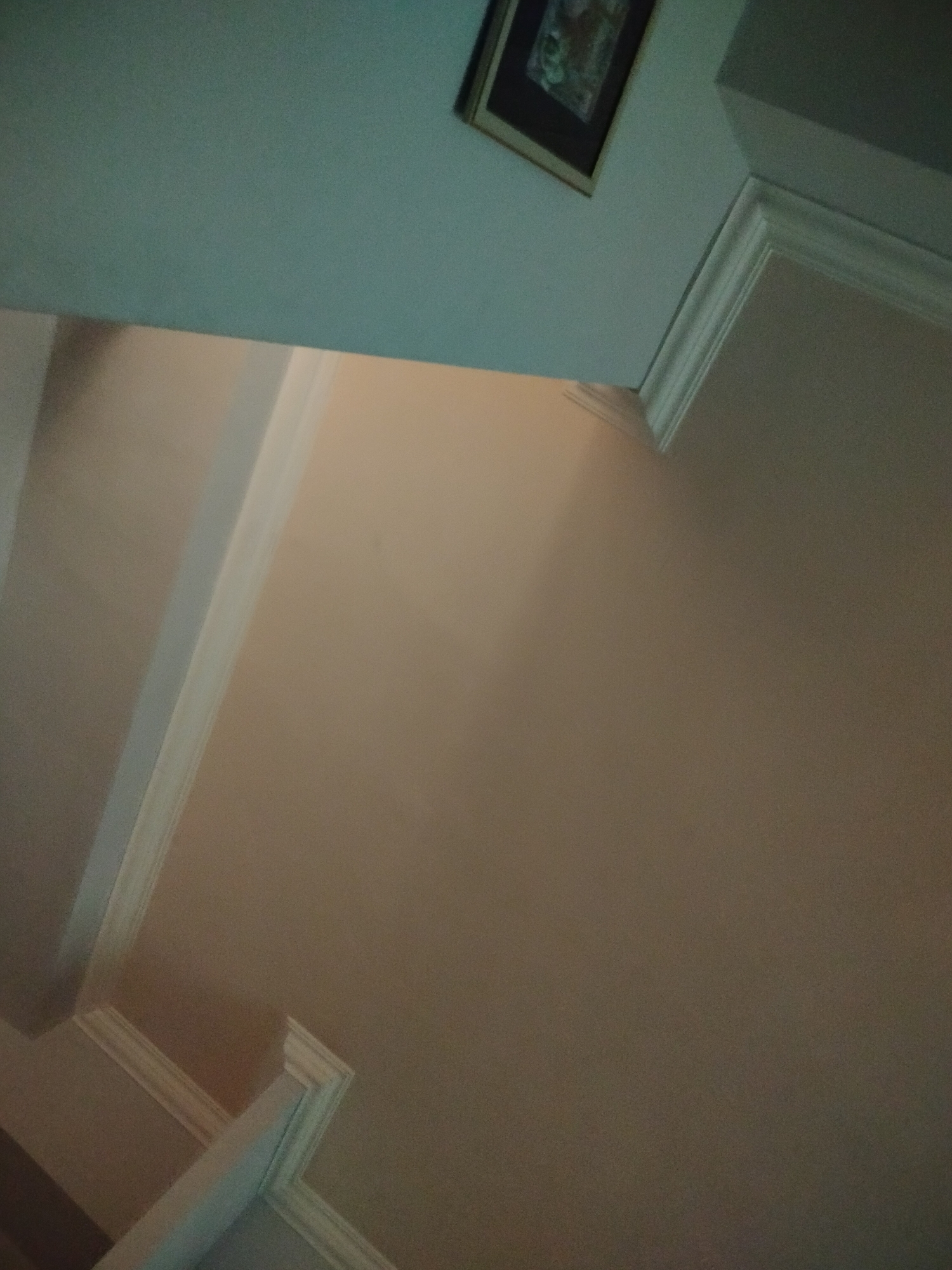 The image shows an interior view of a room, likely a residential space, with a focus on the ceiling and upper walls. The color palette is muted, with shades of beige and white dominating. Architectural details such as crown molding and trim are visible, suggesting a traditional or decorative style. A framed picture hangs on the wall near the ceiling. The overall perspective is slightly angled, giving a sense of depth to the image. There's no clear indication of the location being Yerevan, Armenia.