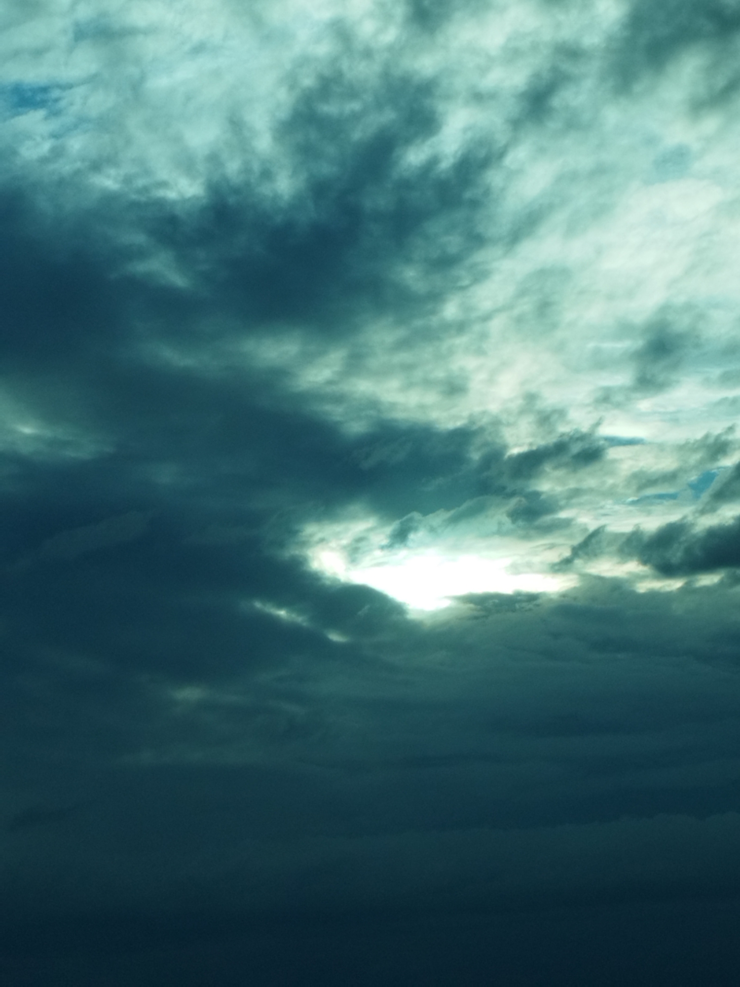 The image depicts a sky filled with dark, moody clouds, with a bright shaft of light breaking through the overcast. The scene is likely located in or around Mircea Vodă, Romania, given the context. There are no people, subjects, or specific objects visible in the frame, only the natural environment of the sky and clouds. The lighting suggests a dramatic or transitional weather condition, possibly before or after a storm. The overall impression is one of atmospheric intensity and subdued natural beauty.