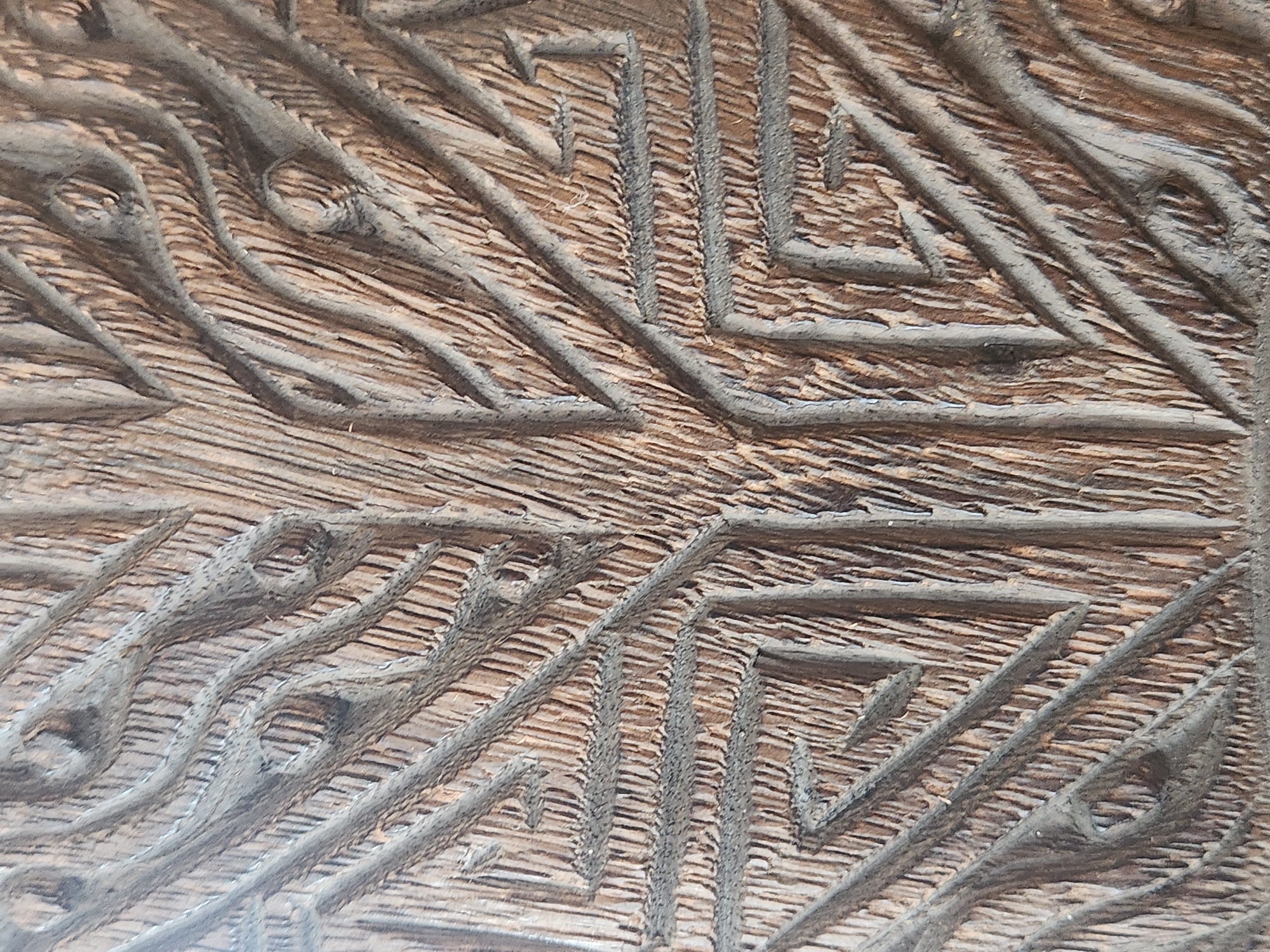 The image is a close-up, overhead shot of a carved wooden surface. The carving depicts an abstract, geometric pattern with organic, tree-like elements. The wood appears aged and weathered, with visible grain and texture. The carving features deep lines and grooves, creating a sense of depth and dimensionality. The overall color palette is dominated by earthy browns and grays, with some lighter highlights and darker shadows.
This image does not contain any identifiable landmarks or contextual information that would allow for its location to be determined within the city of Maitland, United States of America, or any other specific geographic location. Therefore, no location details can be provided.