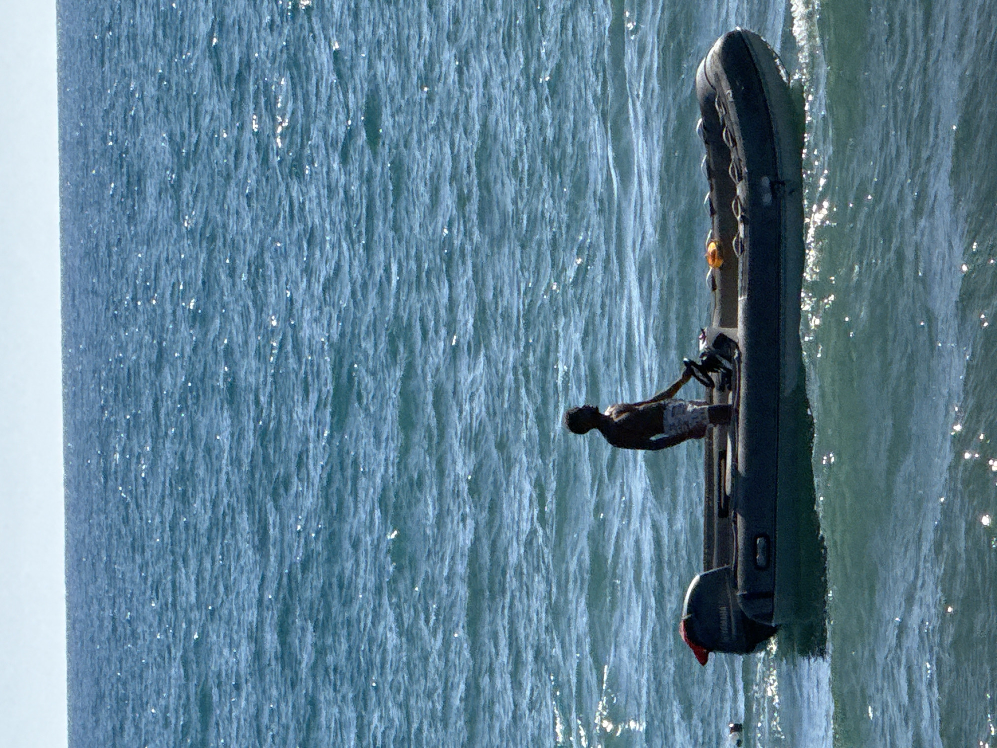 An image of a person driving a small boat on the water. The scene shows the boat moving across the water with the driver in control. The background is mostly ocean, with the sky on the left. Alanya, Turkey is not identifiable in this image.