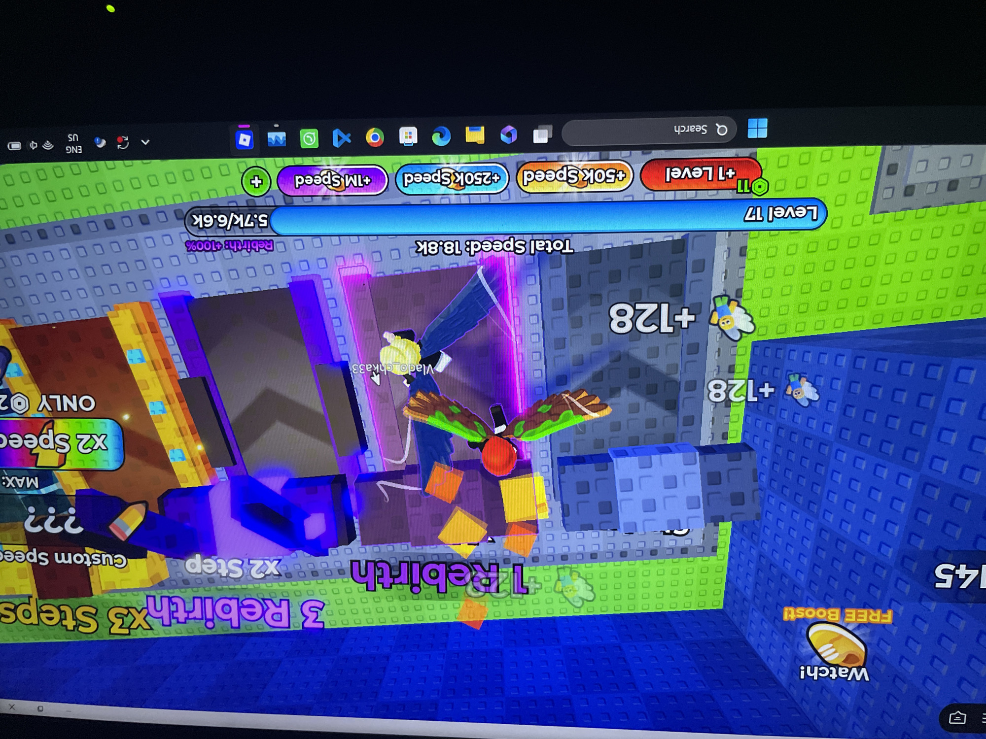 The image shows a screenshot of a video game, likely a Roblox game, displaying a vibrant, colorful in-game environment. The scene features various UI elements common in simulation and upgrade-based games, such as level indicators, currency counters, and upgrade buttons.
Key elements visible in the screenshot include:
* **Level Display:** "Level 17" is prominently displayed.
* **Currency/Points:** "+128" is shown twice, indicating some form of in-game currency or points.
* **Speed Stats:** "Total Speed: 18.8k" is visible, along with buttons to increase speed like "+50k Speed", "+250k Speed", and "+1M Speed".
* **Rebirth System:** "1 Rebirth" and "3 Rebirth x3 Steps" suggest a rebirth mechanic for progression. There's also a "Rebirth: +100%" indicator.
* **Player Avatar:** A player character with a red head and green wings is visible in the center of the screen. Another player avatar with a yellow head is also visible.
* **Boosts and Upgrades:** A "FREE Boost!" option with a shoe icon is present, as well as "x2 Step" and "Custom Speed ???" options.
* **Environment:** The game world appears to be constructed with blocky textures, typical of Roblox, with bright blue, green, and purple platforms.
The image is a screenshot taken from a computer screen, as indicated by the presence of the Windows taskbar at the bottom, showing icons for applications like Google Chrome, Microsoft Edge, and various other system icons.
There is no information within the image that can be used to determine its location in Iyafin, Nigeria. The content is entirely within a digital, virtual game environment.