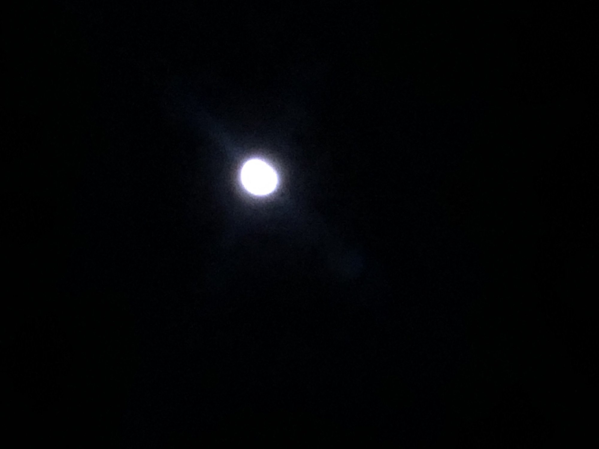 The image is a photograph of the moon in a dark night sky. There is no indication of the city of La Paz, Bolivia, or any other specific location in the image. The moon is a bright, circular object with a slight glow or lens flare around it. The rest of the image is pure black, indicating a very dark environment with no other discernible features. There are no people, objects, actions, or interactions visible in the photograph.