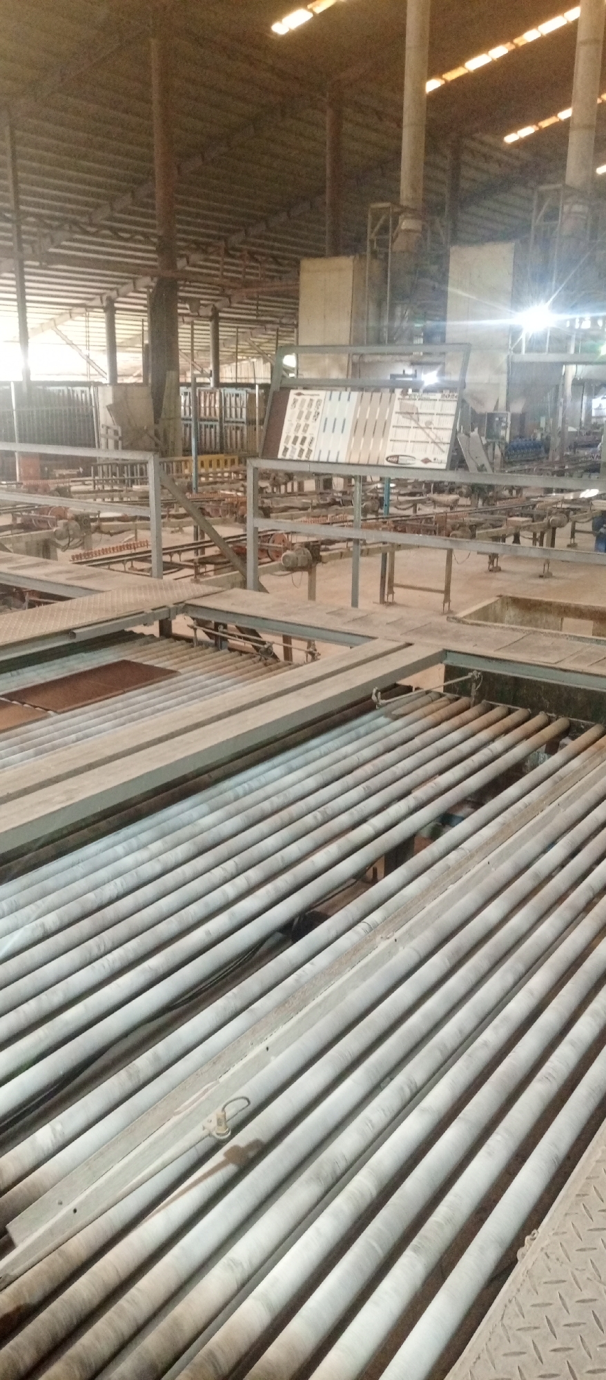 The image depicts the interior of a factory or industrial facility, possibly located in Magboro, Nigeria, based on context. The scene is dominated by a complex network of metal rollers, conveyors, and platforms. There are no people visible. The focus is on the industrial machinery and the general environment. The lighting is subdued, possibly natural light filtering through the roof. The scene suggests a production or manufacturing setting.