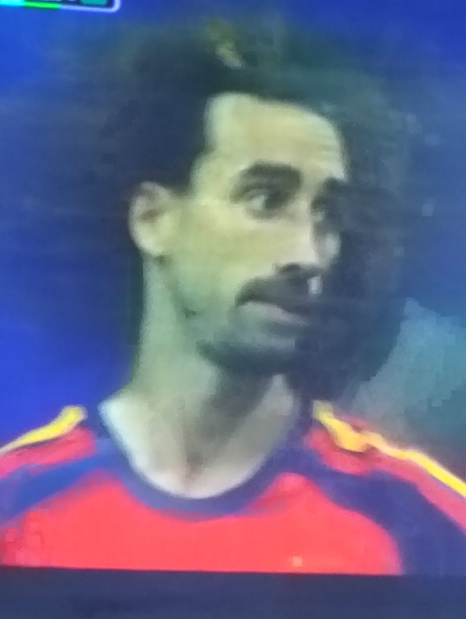 A person with dark, curly hair is looking to the right. They are wearing a red shirt with yellow and blue accents on the collar and shoulders. The background is a dark blue. There is no indication of the city of Payagaboh, Indonesia.