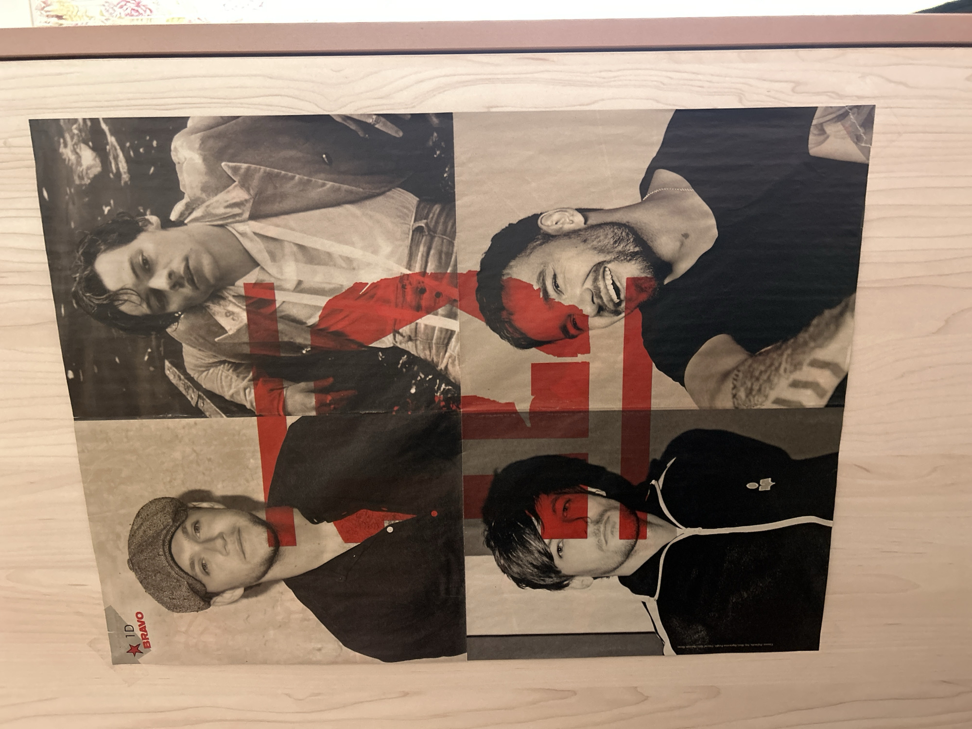 The image shows a poster of the boy band One Direction. The poster is divided into four sections, each featuring a different member. The poster has a red "X" design across the faces. The poster appears to be placed on a wooden surface. No information about the city of Varna, Bulgaria is depicted in the image.
