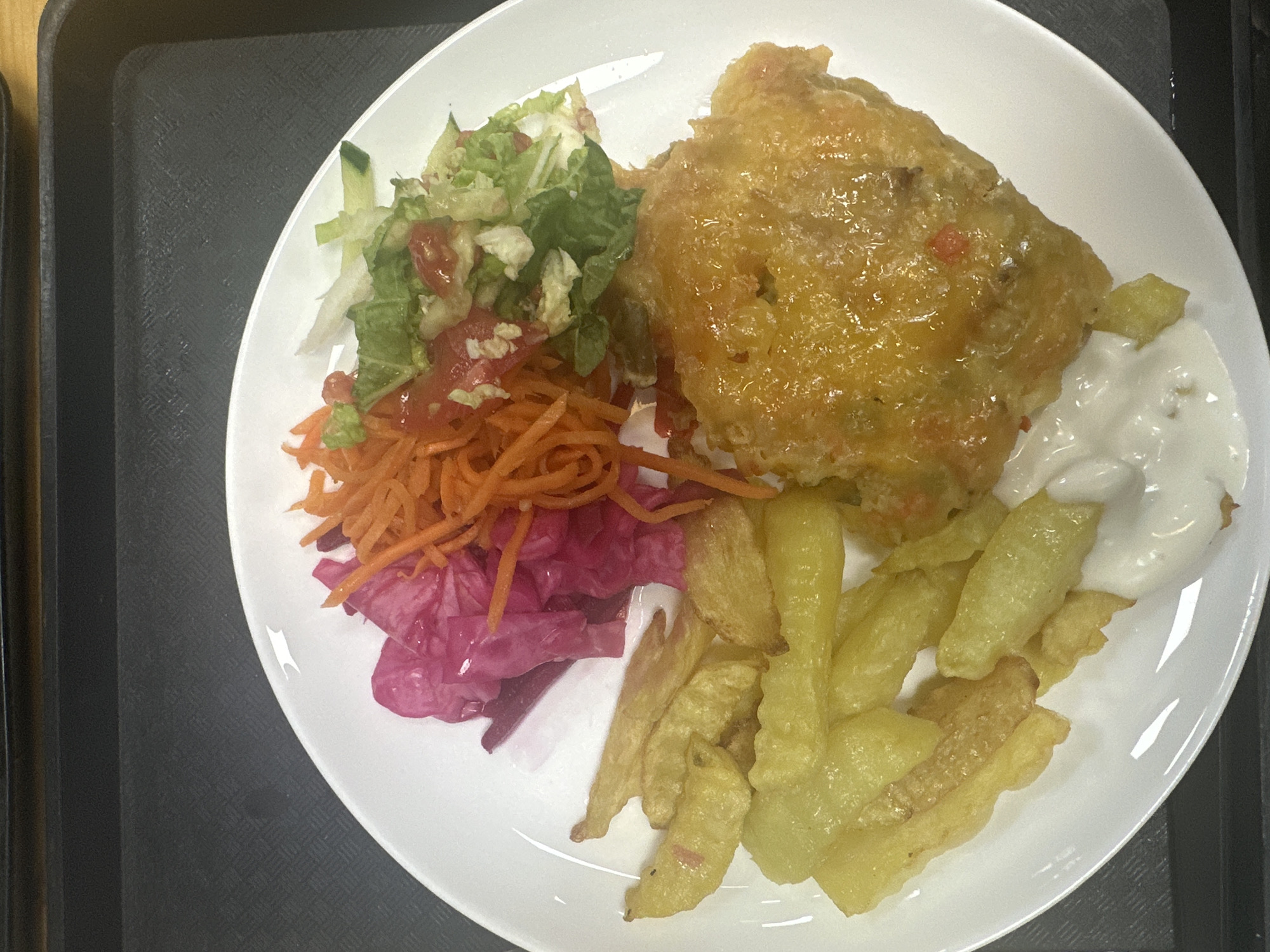 A plate of food sits on a black tray. The food consists of a breaded cutlet, french fries, a dollop of white sauce, and a side salad comprised of shredded carrots, cabbage, lettuce, and tomato. The location is Saint Petersburg, Russia.