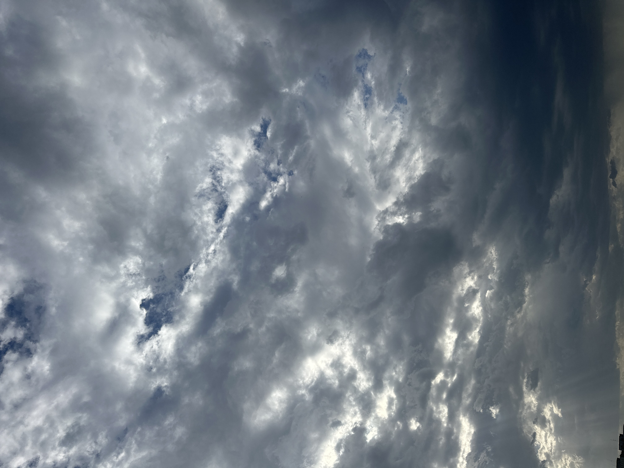 The image shows a sky filled with gray and white clouds. There are a few patches of blue sky visible through the clouds. The location appears to be in the city of Unknown, Unknown. The scene is overcast, and there are no people or objects visible other than the clouds.