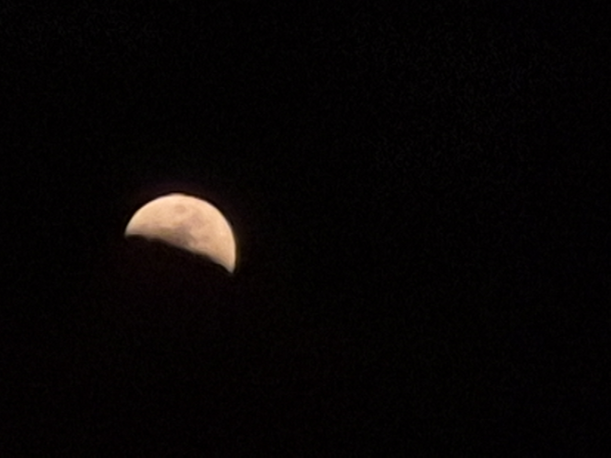 The image shows a crescent moon against a black night sky. The moon is illuminated from the right side, and its surface exhibits some texture. The black background suggests the absence of other light sources, such as city lights or stars, though there are subtle speckles visible which might be noise or distant celestial objects. There are no people, buildings, or any other elements indicative of a specific location within the city of Pernik, Bulgaria, or any other urban environment. The image is a simple astronomical photograph.