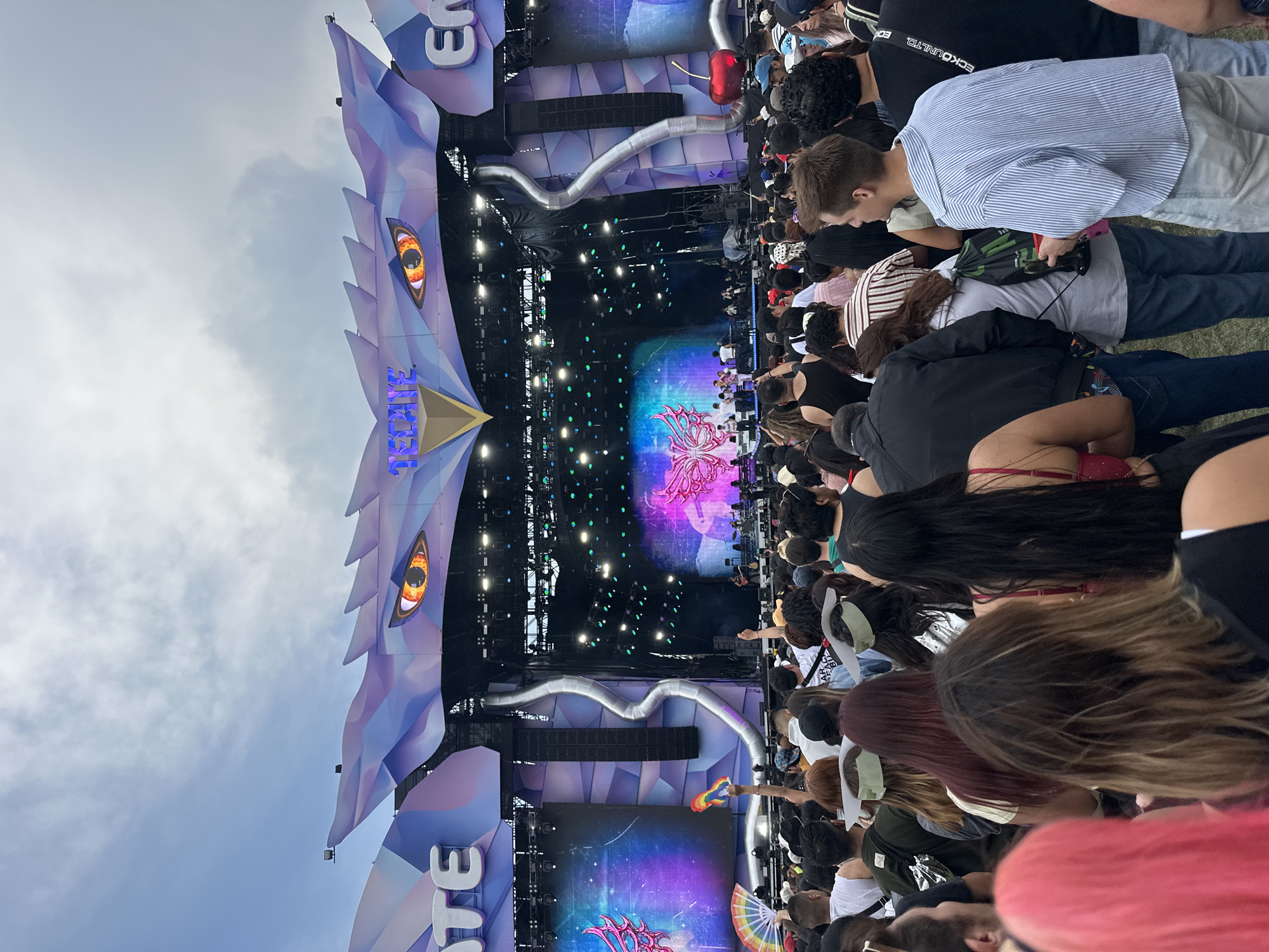 The image shows a crowd of people at a concert, facing a stage with a large, elaborate dragon-themed design. The stage displays the word "ELECTRIC" and features lighting and visual effects. The sky is cloudy. The event appears to be taking place outdoors in Mexico City, Mexico.