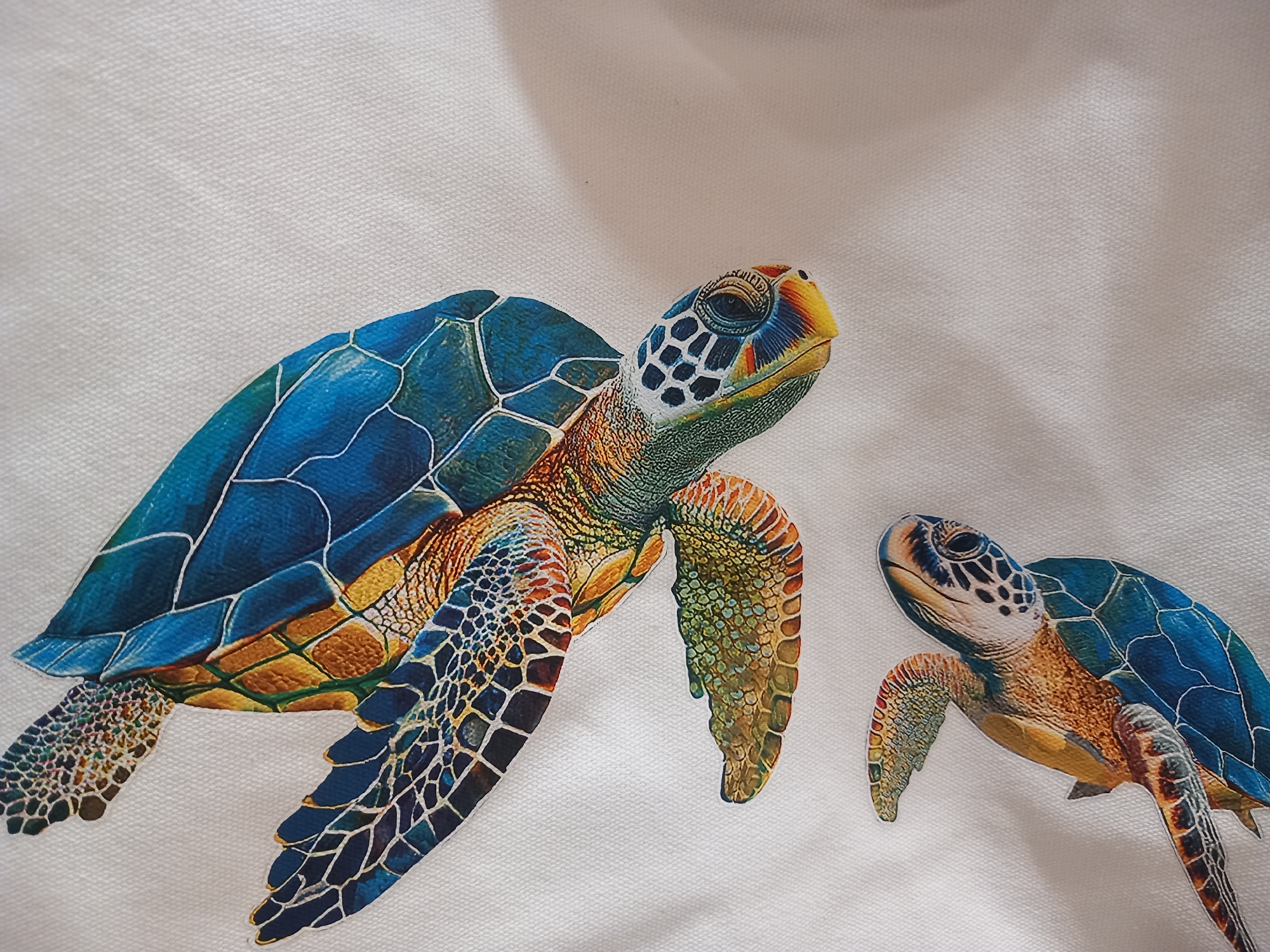 This media file features a close-up, slightly angled shot of two illustrated sea turtles on a textured, off-white background that appears to be fabric. The larger turtle is positioned in the foreground, its body angled to the right, with its head and front flipper prominently displayed. It has a vibrant blue shell with distinct hexagonal patterns outlined in white. Its skin is a mix of green, orange, and brown, with intricate scale details. The smaller turtle is situated in the middle ground, to the right of the larger one, facing towards the left. It shares similar coloration and patterning to the larger turtle. The background shows subtle shadowing and texture, suggesting it might be a canvas or a woven material. The lighting appears soft, possibly indicating an indoor setting or diffused natural light, and there are no obvious cues about the time of day, weather, or specific location. The overall mood is artistic and serene, focusing on the detailed rendering of the marine animals. There is no visible text in the image.
