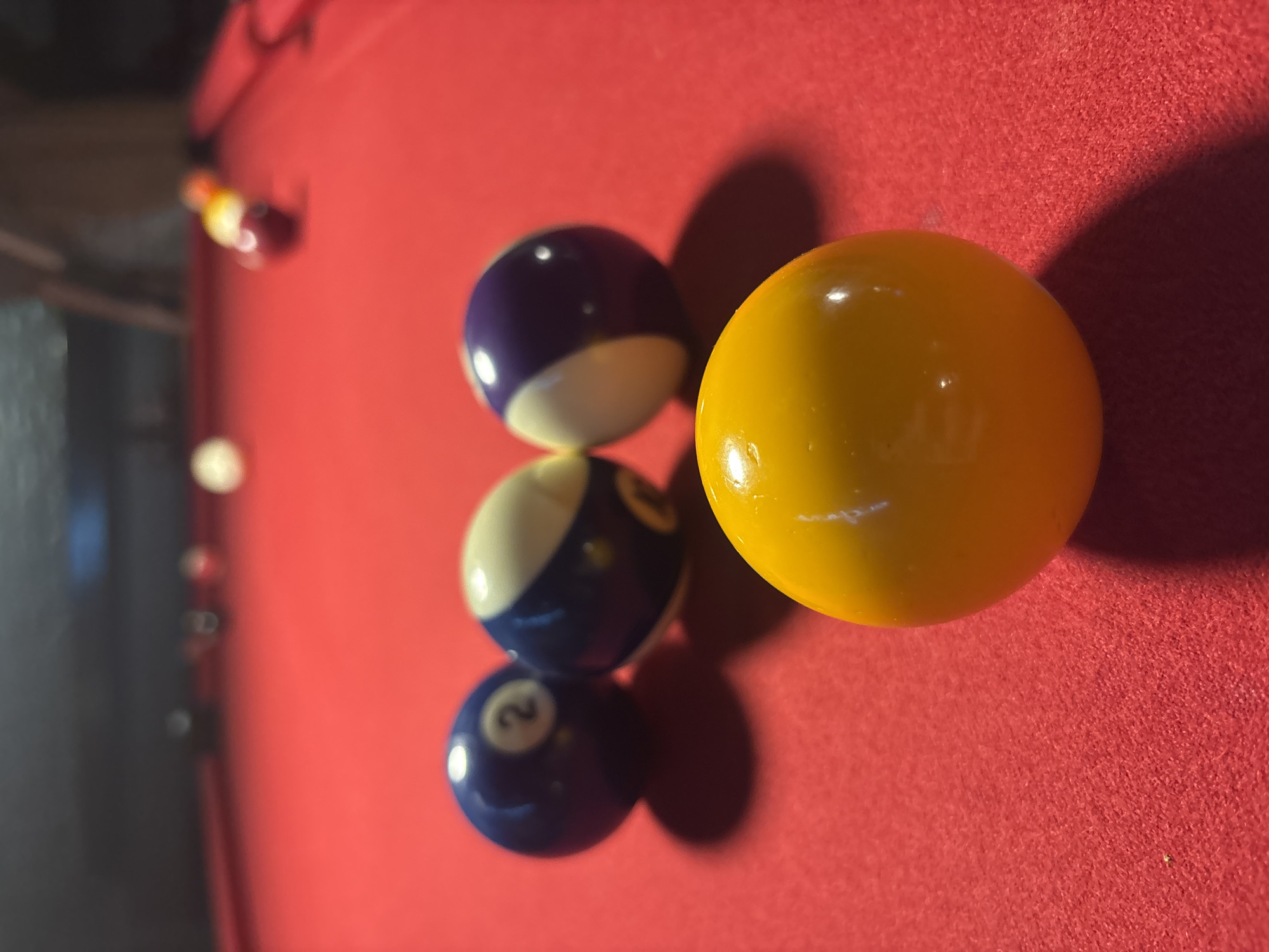 The image shows a close-up of a billiards table with a red felt surface. There are four pool balls in the frame. A yellow ball is positioned to the right, and three other balls are stacked vertically on the left side. From top to bottom, these are a purple and white ball, a blue and white ball (eight-ball), and a blue ball with the number 2 on it. The location in Mexico City, Mexico, cannot be determined from the information in the image.