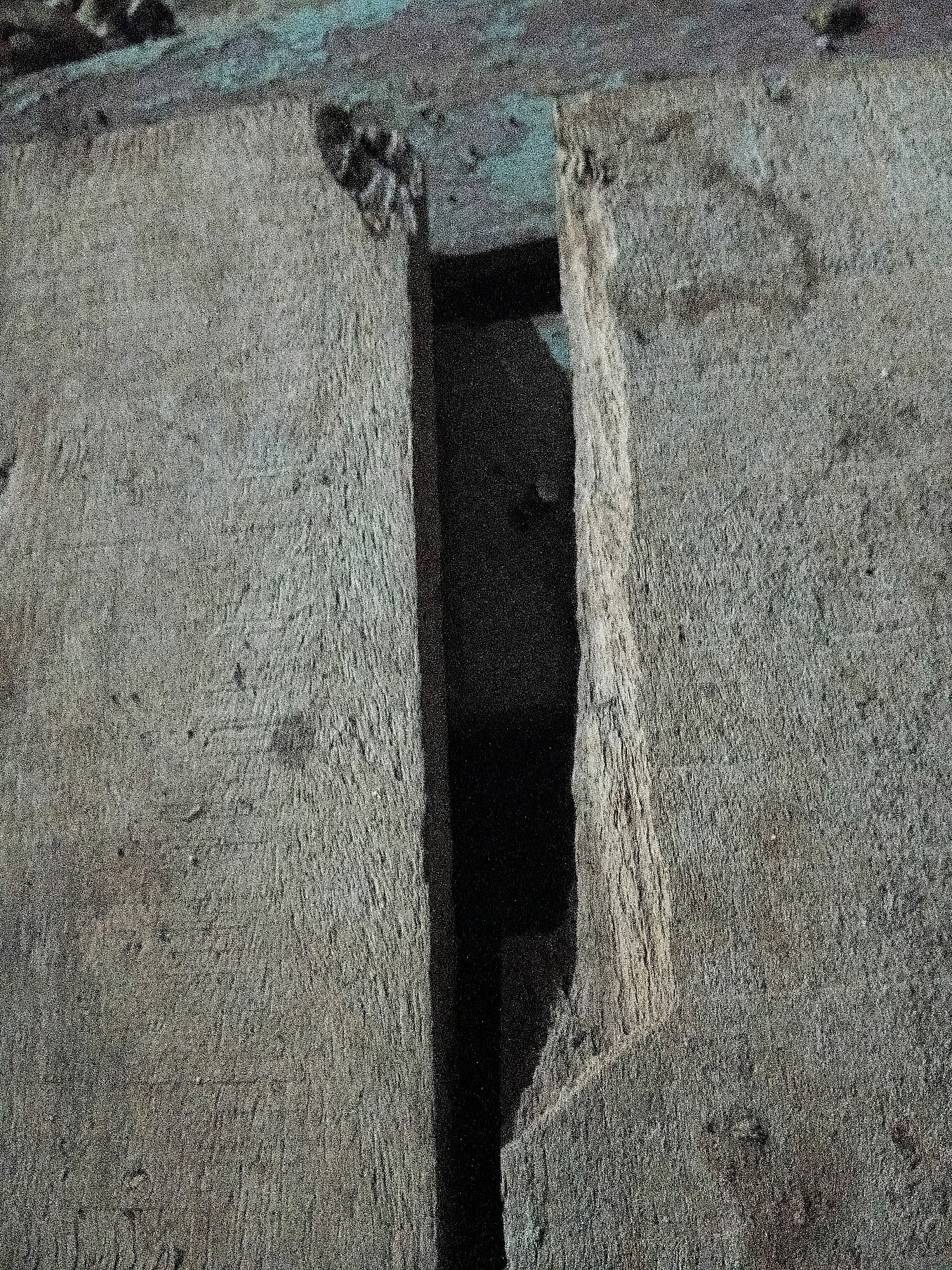 The image shows a close-up view of a cracked concrete structure. A narrow, dark gap runs vertically through the center of the frame, dividing the concrete into two distinct sections. The concrete surfaces are rough and textured, with visible signs of wear and tear. The lighting suggests an outdoor environment, possibly in an urban setting. The specific location in Cikal, Indonesia is not discernible from the image.