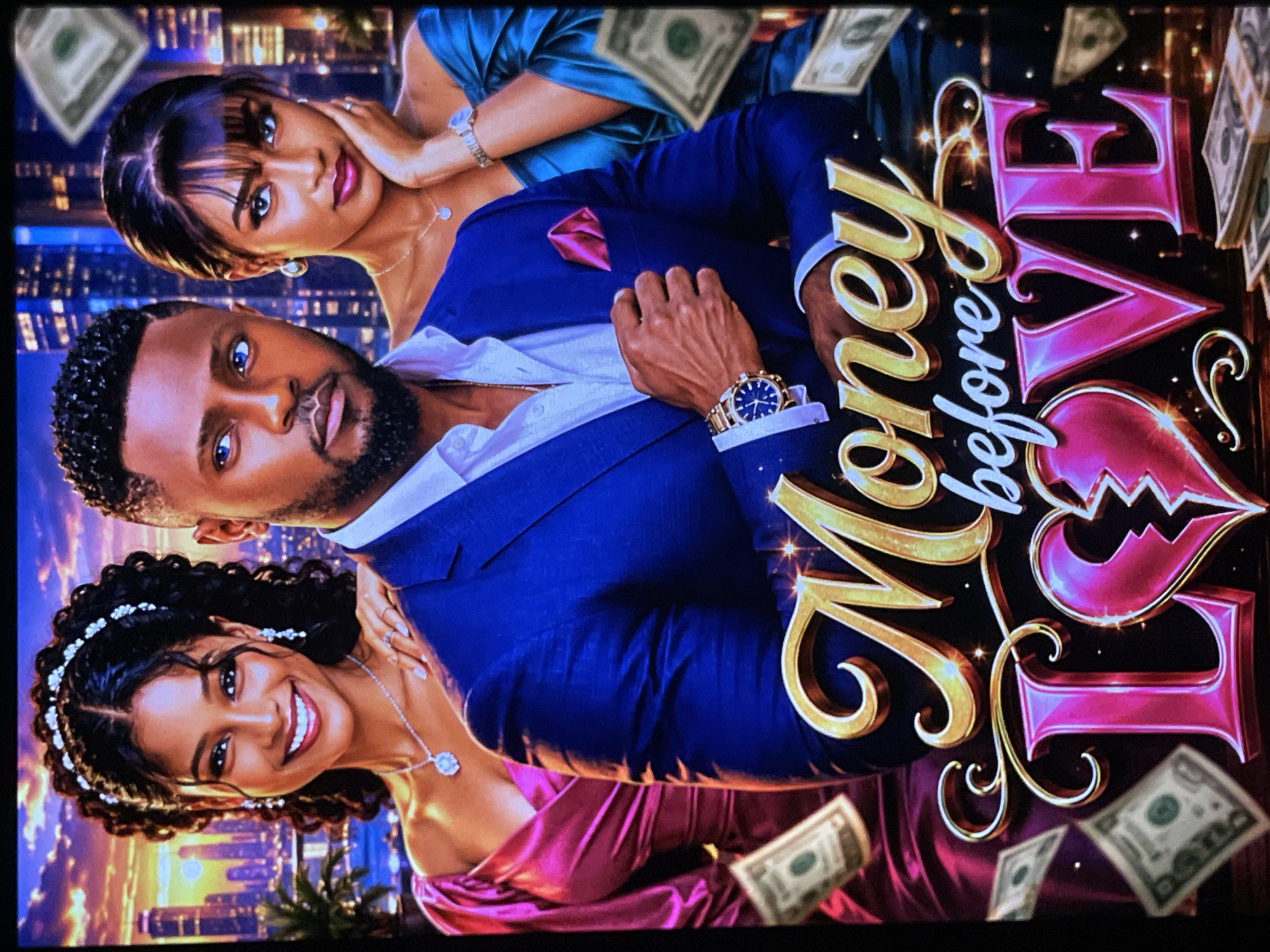 A movie poster titled "Money Before Love" features a man in a blue suit and two women in elegant dresses. The man stands in the center, looking forward with a serious expression. To his left, a woman in a pink dress smiles broadly, adorned with a tiara and jewelry. To his right, a woman in a teal dress gazes towards the viewer, resting her hand on her cheek. The background depicts a cityscape at night, with glittering buildings and lights. Scattered dollar bills surround the subjects, emphasizing the film's theme. The title is prominently displayed in large, stylized golden and pink lettering, with the word "LOVE" featuring a broken heart graphic.