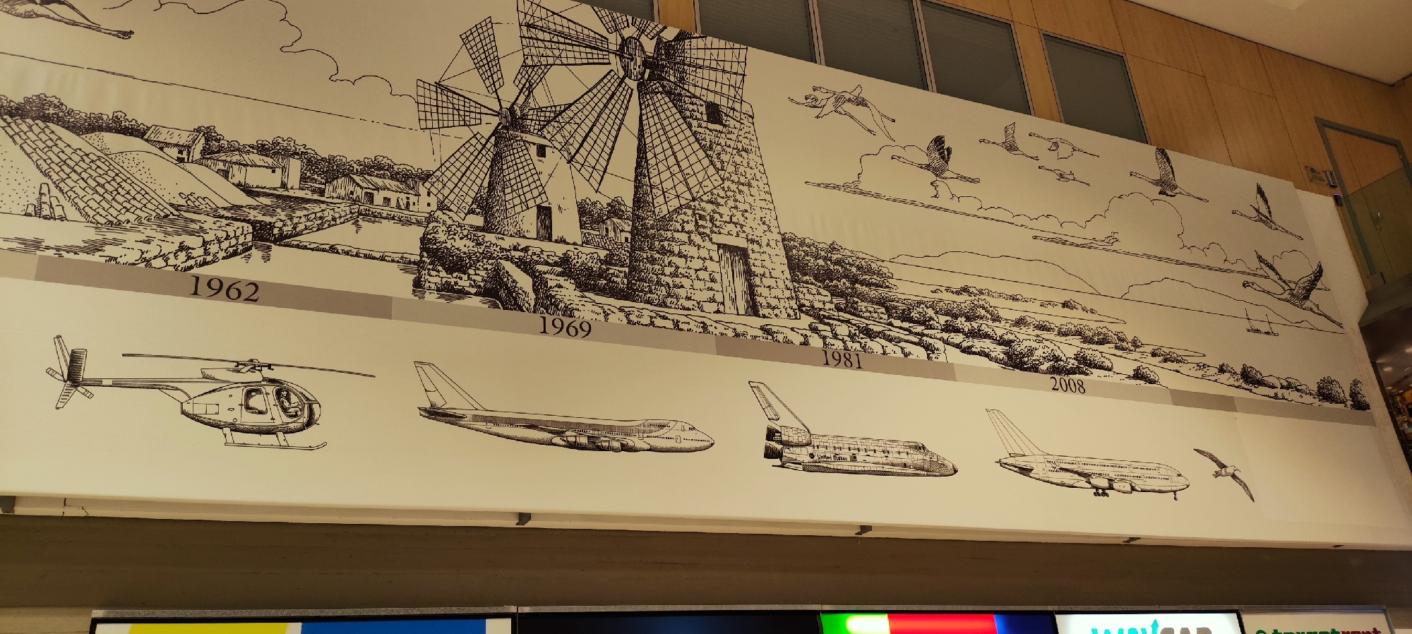 The image is a mural depicting the history of flight, with a timeline marked by years: 1962, 1969, 1981, and 2008. The upper portion of the mural shows a landscape with traditional windmills and birds in flight. The lower portion illustrates various aircraft from different eras, including a helicopter, a large passenger jet, a space shuttle, and another large airplane. A seagull is also depicted in flight next to the last airplane. The mural is located in Marsala, Italy. The overall scene is a detailed, hand-drawn representation of technological advancements in aviation against a historical and natural backdrop.