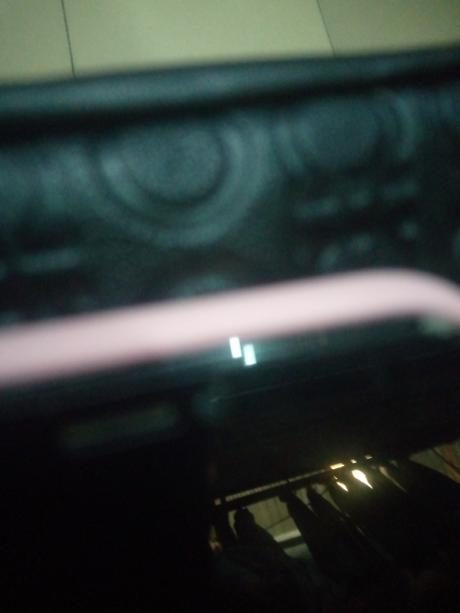 The image shows a close-up, out-of-focus view of what appears to be electronic equipment, possibly a stereo or audio mixer, with a pinkish-white cable or handle running across the foreground. There are some illuminated rectangular shapes or buttons visible on the equipment. The background is dark and indistinct, suggesting low lighting conditions. The scene is not identifiable as being in Jalingo, Nigeria.