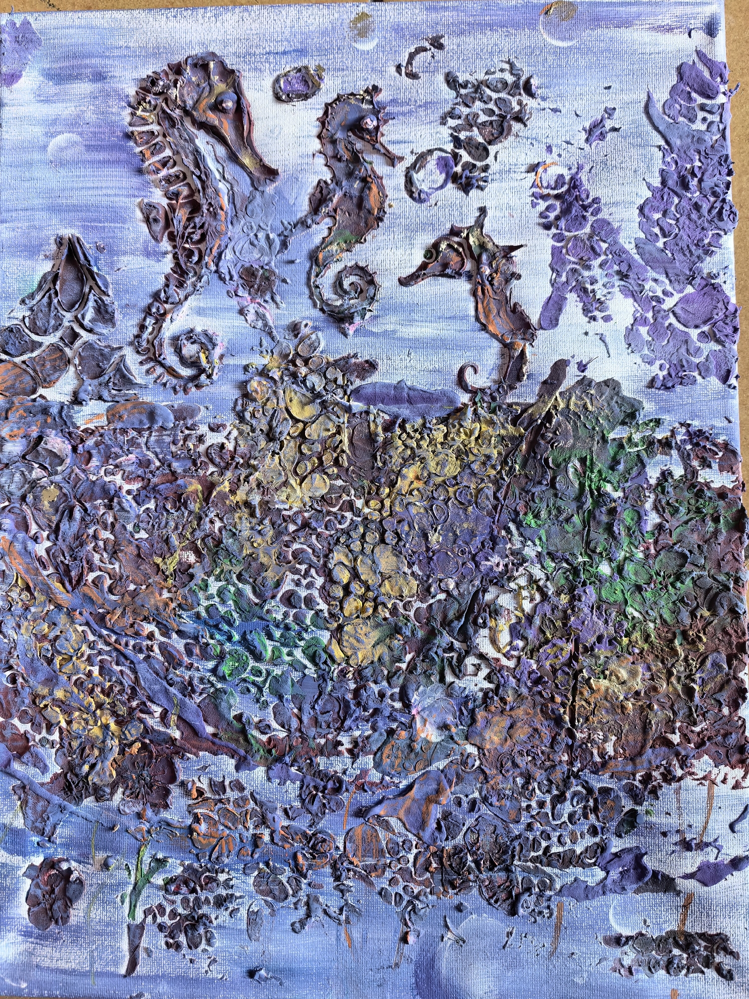 The image is an abstract textured painting of seahorses in an underwater environment. The painting is predominantly composed of thick impasto textures in shades of purple, blue, green, brown, and gold. Three seahorses are distinctly visible in the upper portion of the painting, positioned against a lighter blue background suggestive of water. The seahorses are depicted in various postures and orientations. Below the seahorses, a densely textured area represents the seabed or coral reef. The bottom of the painting continues the blue color scheme with textured brushstrokes. There are no people visible in the image. The location is underwater, which suggests a marine environment, but not identifiable with a specific city or location.