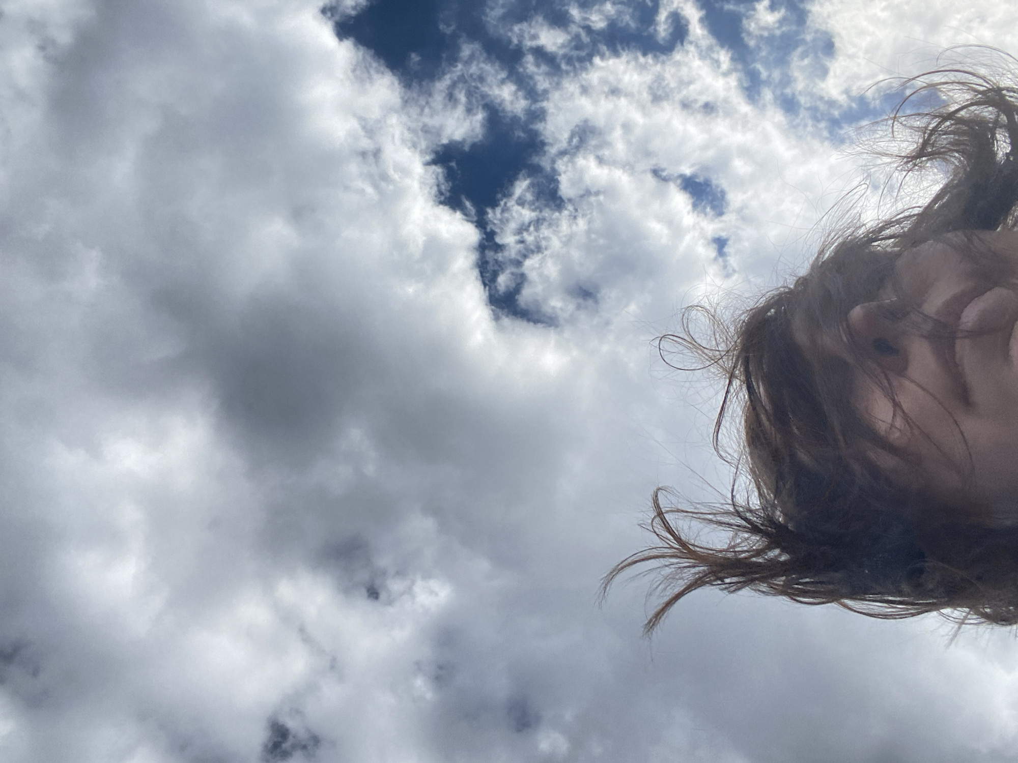 The image depicts a low-angle view of a cloudy sky with a small patch of blue visible in the upper portion. Part of a person's face and hair is visible in the right side of the frame, seemingly captured from below. The location is not discernible from the visual content of the image. The city of Nizhnie Yaki, Russia, cannot be verified as the location based on the provided image.