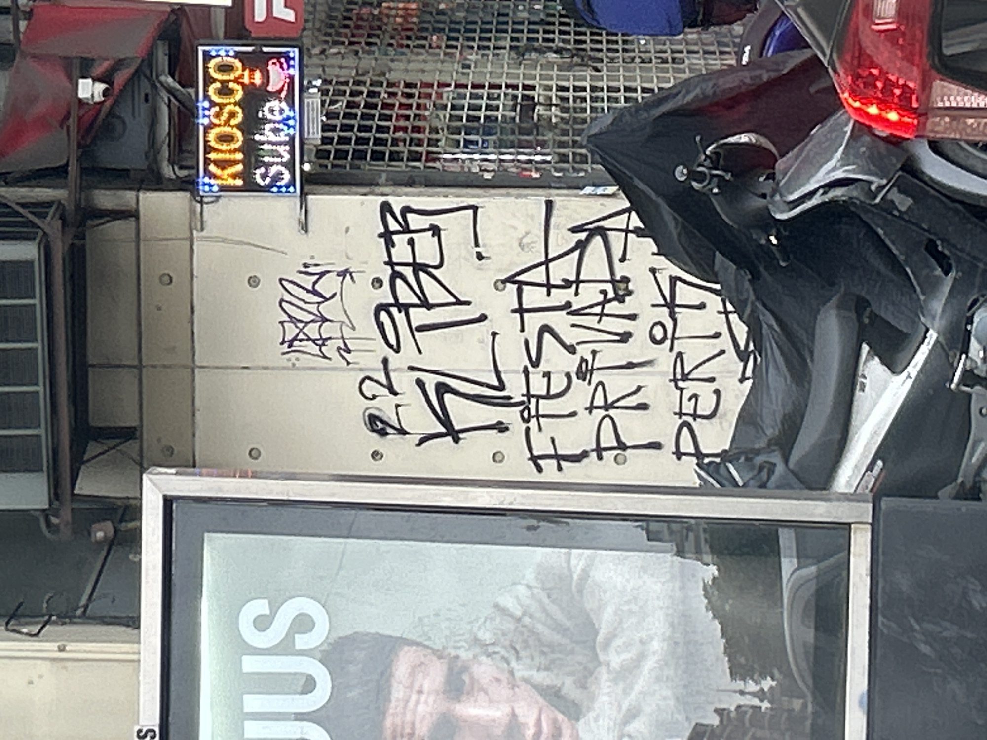 The image shows a street scene in Buenos Aires, Argentina. A "Super KIOSCO" sign is visible above a building facade covered in graffiti. A motorcycle is parked in front of the building, partially obscuring the graffiti. A poster or advertisement is visible below the graffiti. The overall environment appears urban and somewhat rundown.