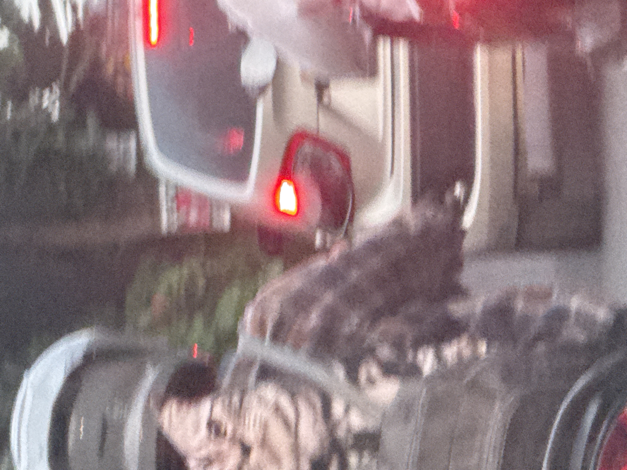 A blurry, rotated image shows a vehicle, possibly a truck, on a road in Baturiti, Indonesia. The vehicle is predominantly white, with red rear lights illuminated. There are visible trees and vegetation to the side of the road. The image quality is poor, making finer details unclear.