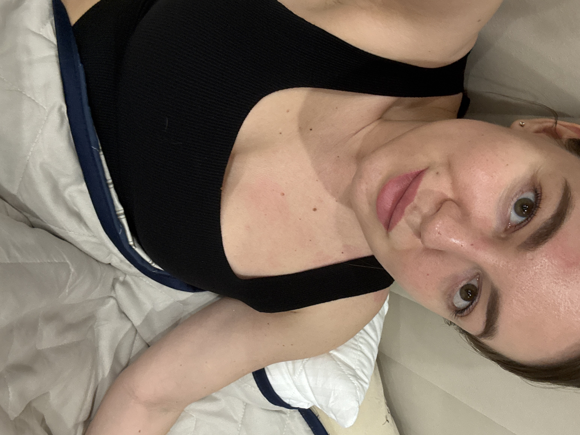 A woman with light skin and brown eyes lies on a quilted bed, wearing a black top. The setting appears to be indoors, possibly in a residential space. There is no information to indicate that the image was taken in Orekhovo-Zuyevo, Russia.