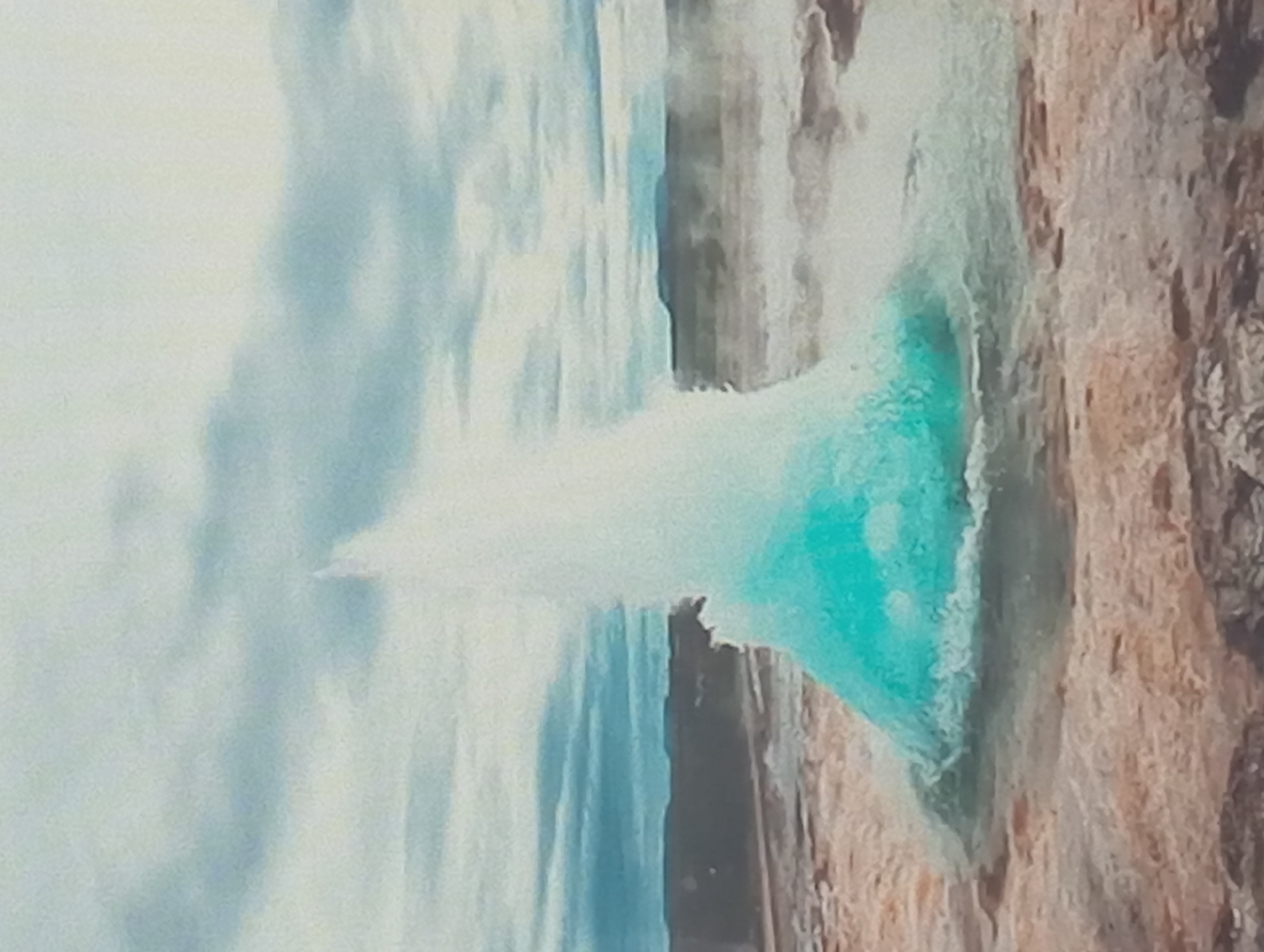 The image depicts a geyser erupting. Water is shooting upwards in a white plume, with a turquoise hue in the pool. The geyser is surrounded by rocky terrain. In the background, there is a cloudy sky. The image is rotated ninety degrees.
It is not possible to determine whether this image is related to Karaganda, Kazakhstan, from the image itself.