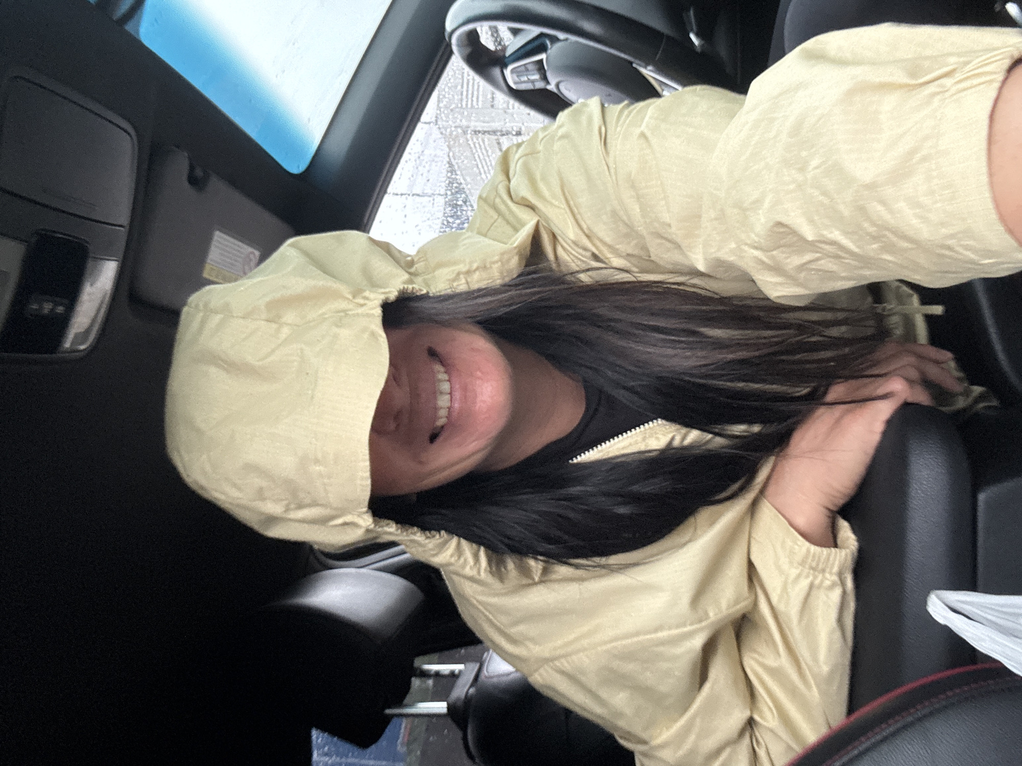 A person is in the driver's seat of a car. The person is wearing a hooded jacket. Rain is visible on the windshield. The specific location in Chaikovsky, Russia cannot be determined from the image.