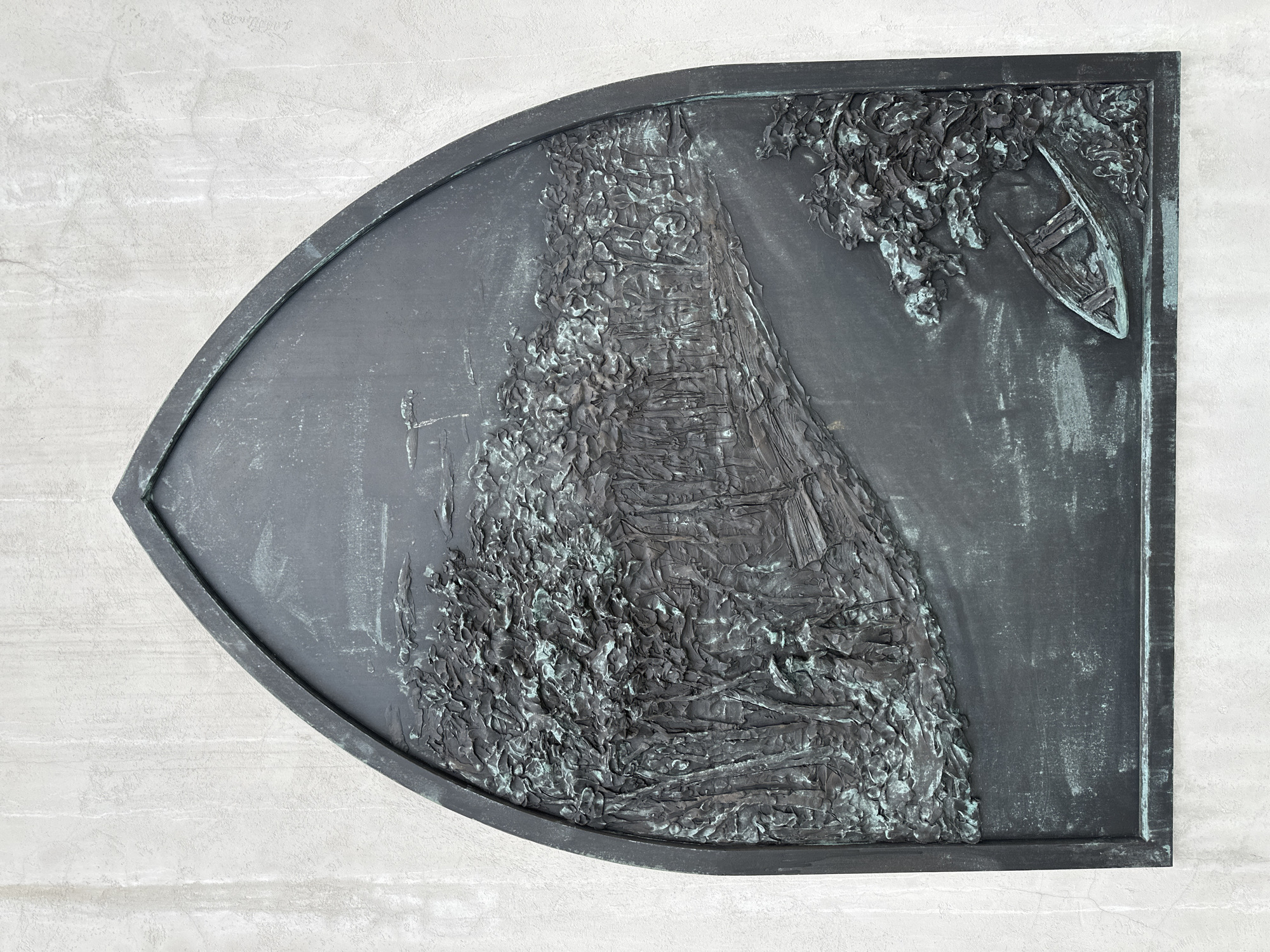 This is a bronze relief mounted on a rough, light-colored wall, likely concrete or stucco. The relief is framed by an arched top and rectangular bottom, resembling a gothic window shape. The scene depicted is a stylized landscape.
In the foreground, a path or road winds from the lower left towards the upper right. On the left side of the path, there is a dense forest with textured trees. A few small, human-like figures can be seen among the trees, one of whom appears to be holding an umbrella. On the right side of the path, the landscape is less dense, with some foliage. At the lower right corner of the relief, there is a small, overturned boat partially submerged in what appears to be water, with some vegetation around it. The background of the relief is relatively flat, with some indistinct shapes suggesting clouds or distant features. The bronze has a patina, with areas of green oxidation visible.
This relief is located at the memorial to the victims of the Belarusian state security apparatus (KGB) in Minsk, Belarus, specifically on the wall of the building that was formerly the KGB headquarters.