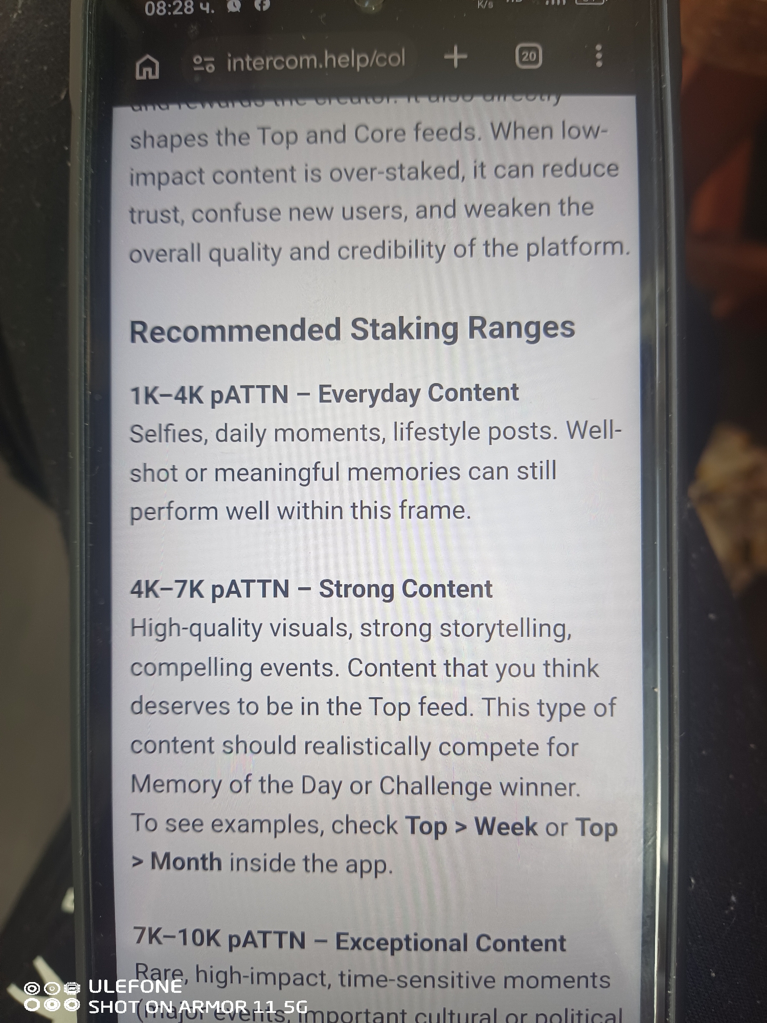 A Ulefone Armor 11 5G smartphone screen, illuminated and slightly angled, displays a webpage from "intercom.help" at 08:28. The screen features a prominent section titled "Recommended Staking Ranges." Under this heading, three content categories are listed: "1K-4K pATTN - Everyday Content" (described as selfies, daily moments, and lifestyle posts), "4K-7K pATTN - Strong Content" (characterized by high-quality visuals, strong storytelling, and compelling events, advising users to refer to "Top > Week or Top > Month" in the app), and a partially visible "7K-10K pATTN - Exceptional Content" (describing rare, high-impact, time-sensitive moments). Preceding text on the screen discusses how over-staking low-impact content can reduce trust and weaken platform credibility. The phone's status bar indicates the time, network connectivity (5G, K/s), and battery level, alongside browser tabs and menu icons. The device rests against a dark, uniform background, with a subtle reflection visible on the screen's right edge.