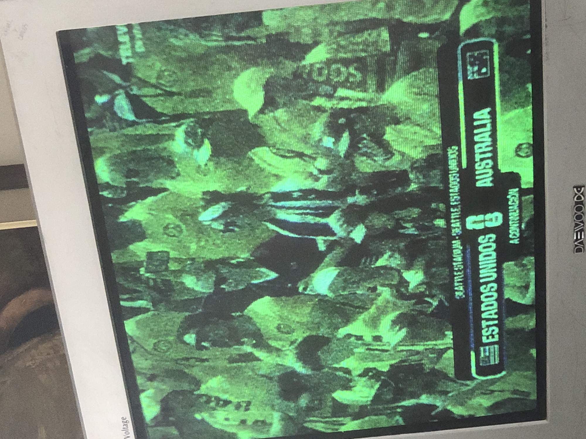 The image is a photograph of a television screen displaying a sports broadcast. The screen is green-tinted, suggesting a color calibration issue or the nature of the broadcast. The broadcast appears to be a soccer match, with team names displayed in a banner at the bottom of the screen: "ESTADOS UNIDOS" (United States) and "AUSTRALIA". The background shows a crowd of people, many wearing green shirts, likely spectators at a stadium. Above the team names, text reads "SEATTLE STADIUM - SEATTLE, ESTADOS UNIDOS". The television itself is an older model, with a visible "DAEWOO" logo at the bottom of the frame. The image is slightly out of focus and has a grainy quality. There is no visual information in the image that would indicate the location in the city of La Tagua, Venezuela.