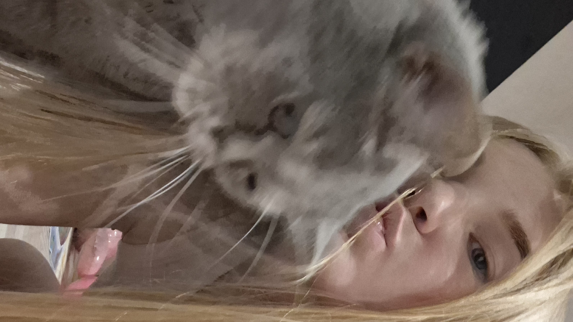 A young woman with blonde hair lies on her back, facing upward and slightly to the right. A chinchilla is perched close to her face, near her mouth. The background is indistinct. There is no evidence to suggest this image was taken in the city of Chaikovsky, Russia.