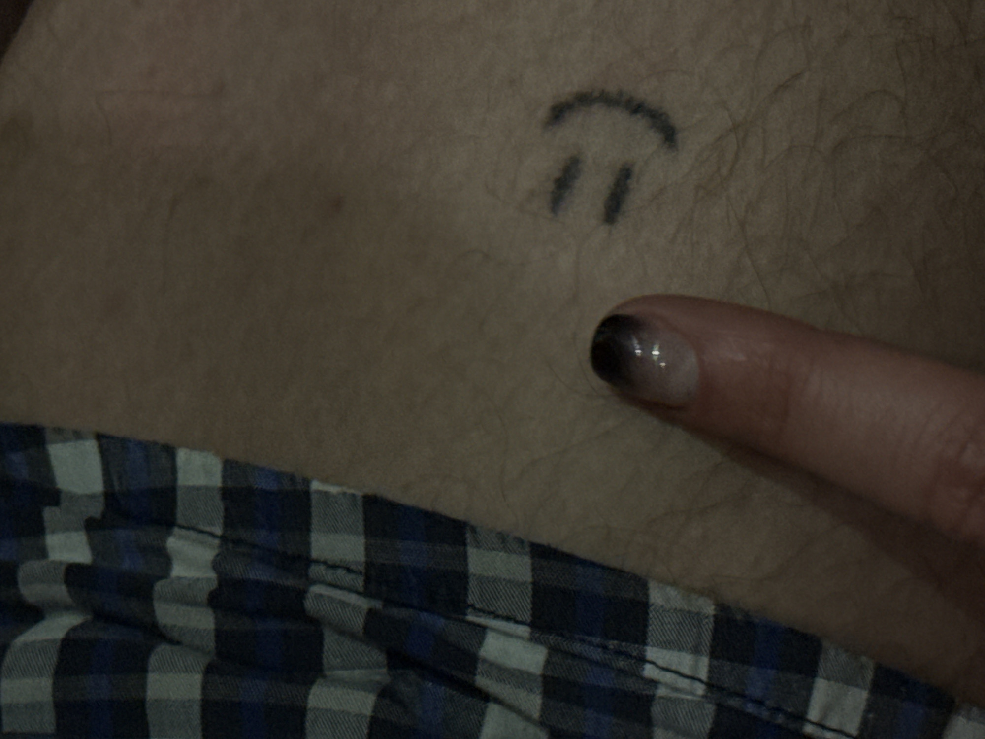 The image shows a person's torso with a simple drawn smiley face on the skin above the waistline. A finger is pointing towards the drawing. The person is wearing a blue and gray plaid shirt or pajamas. The image doesn't contain any information about the location. Therefore, it is impossible to include any mention of Sochi, Russia.