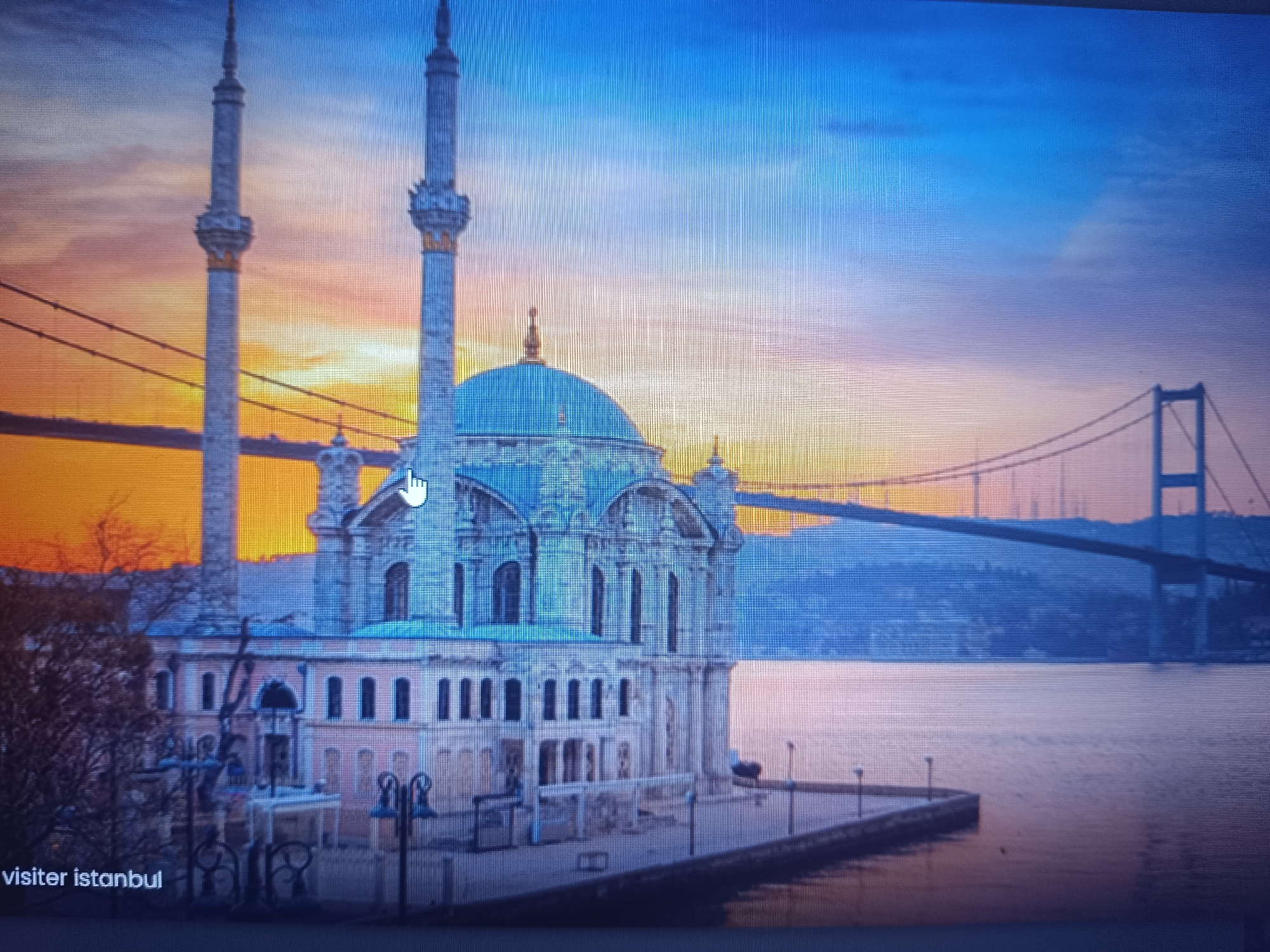 The image depicts the Ortaköy Mosque in Istanbul, Turkey, at sunset. The mosque, with its prominent blue dome and twin minarets, is located on the edge of the Bosphorus Strait. In the background, the Bosphorus Bridge is visible, spanning the strait. The water reflects the colors of the sky, creating a serene and picturesque scene. There are no people visible in the image. The text "visiter istanbul" appears at the bottom left. The image is not related to Seewald, Germany.