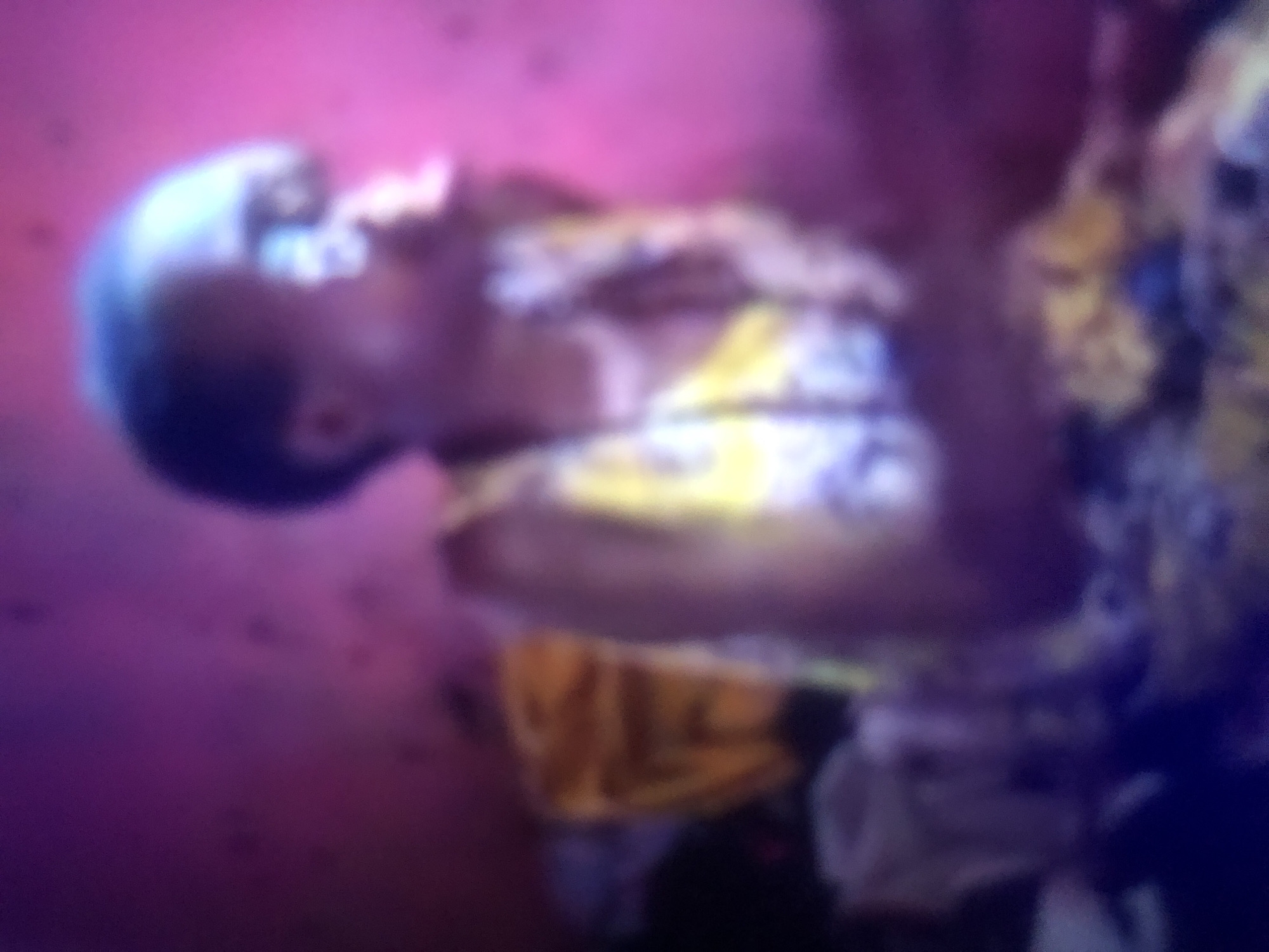 The image shows a young person, likely a child, sitting on a bed. They are wearing a yellow and white patterned garment. The background is a pink wall. The image is blurry and appears to have been taken in low light conditions. The context of "Howayi, Nigeria" is not evident from the visual information provided in the image.