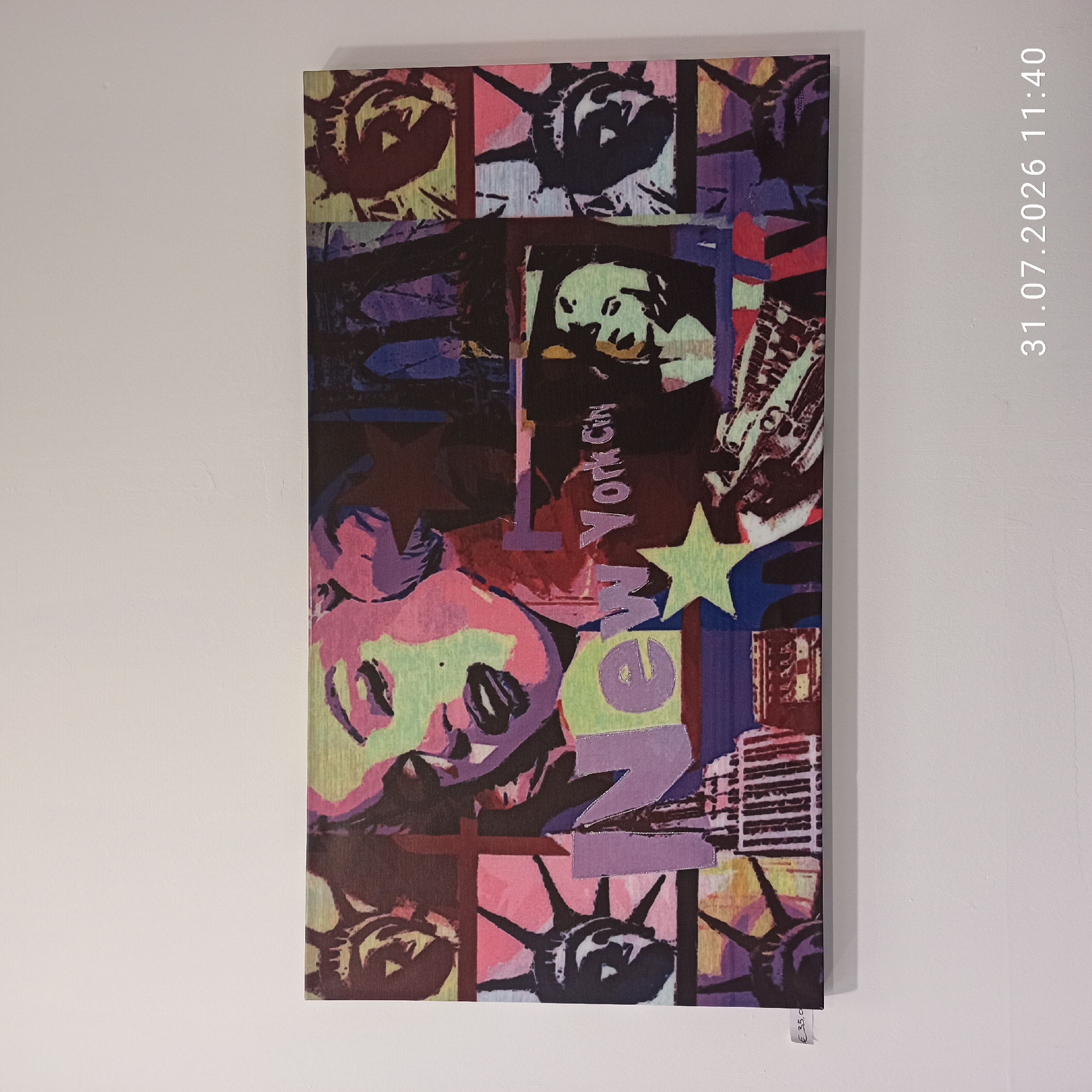 The image displays a pop art-style canvas on a white wall. The canvas is a collage of images, featuring a stylized portrait of Marilyn Monroe, several depictions of the Statue of Liberty, the Empire State Building, and what appears to be US currency. The colors are vibrant and bold, with prominent use of pink, purple, green, and yellow. Text that reads "New York City" is integrated into the artwork, with "New" in large, blocky letters and "York City" in a more script-like font. A price tag with "€ 35,0" is visible on the bottom left corner of the canvas. The lower right corner of the image shows a timestamp: "31.07.2026 11:40". The scene appears to be an indoor setting, likely a shop or gallery, given the price tag and the artwork displayed on a wall. The city of Modugno, Italy, is not depicted in the image itself, nor is there any information provided within the image to associate it with that specific location.