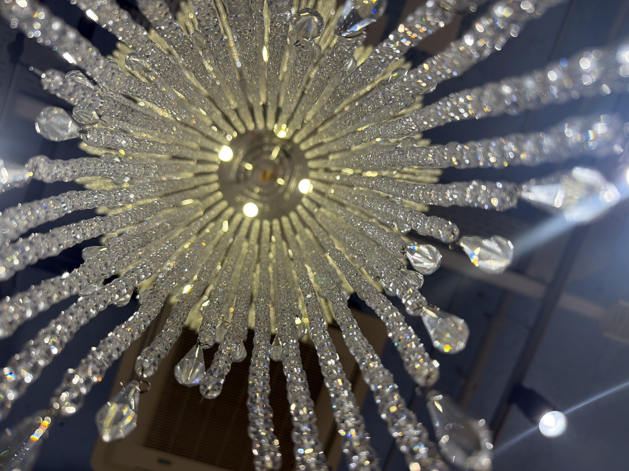 A low-angle shot of a crystal chandelier with multiple tiers and strings of crystals. The light fixture is suspended from the ceiling and the perspective looks upward towards the center, where light bulbs are visible. The crystals refract light, creating a sparkling effect.
I have no information indicating that this image was taken in Spreitenbach, Switzerland.