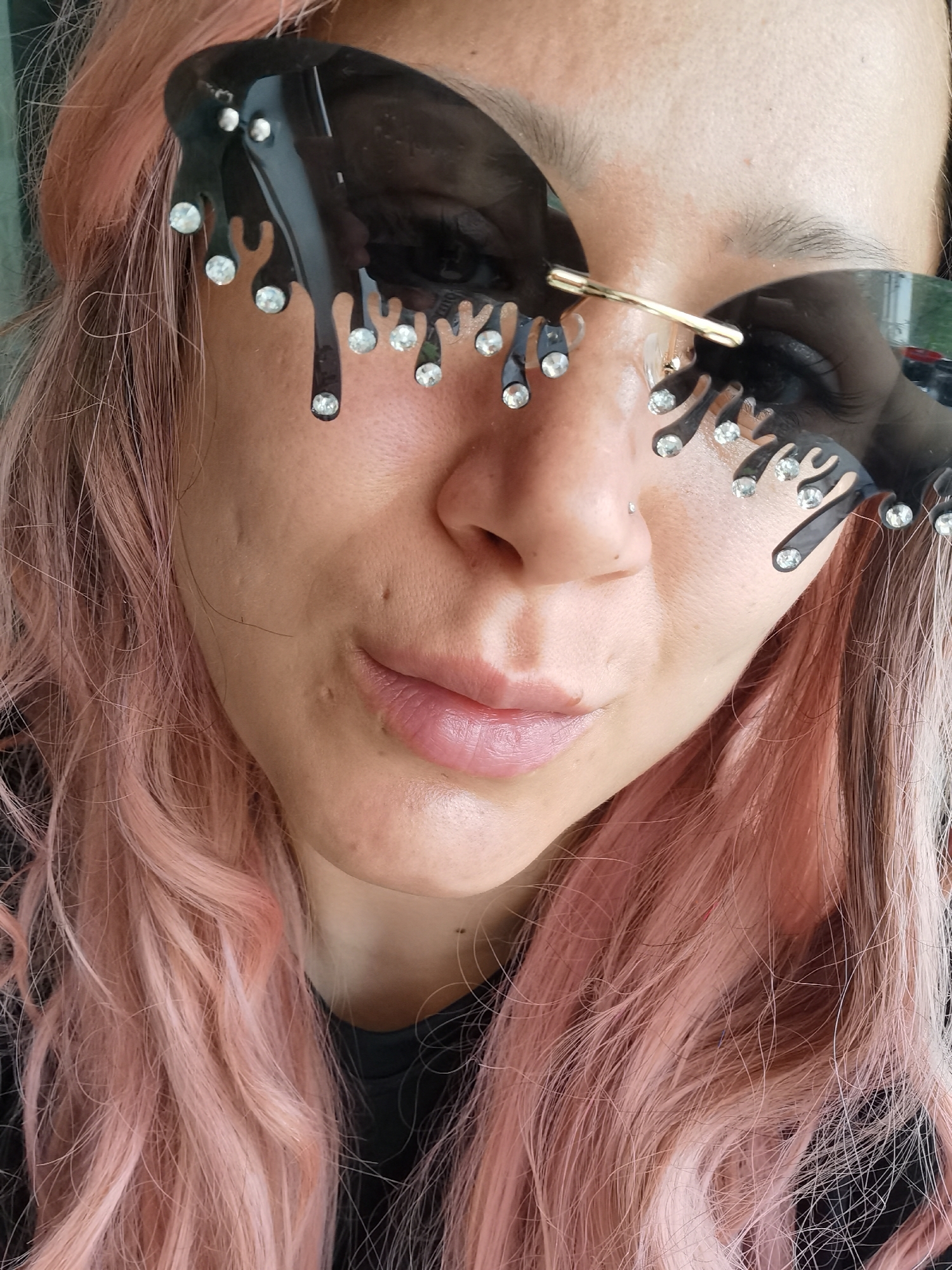 A close-up portrait shows a person with pink hair wearing large, dark sunglasses. The sunglasses feature a decorative, dripping design, embellished with small, clear gems. The subject's skin appears fair, with a visible piercing on the nose. The background is indistinct, and not enough detail is provided to determine the location as Chaikovsky, Russia. The focus is primarily on the person's face and the sunglasses.
