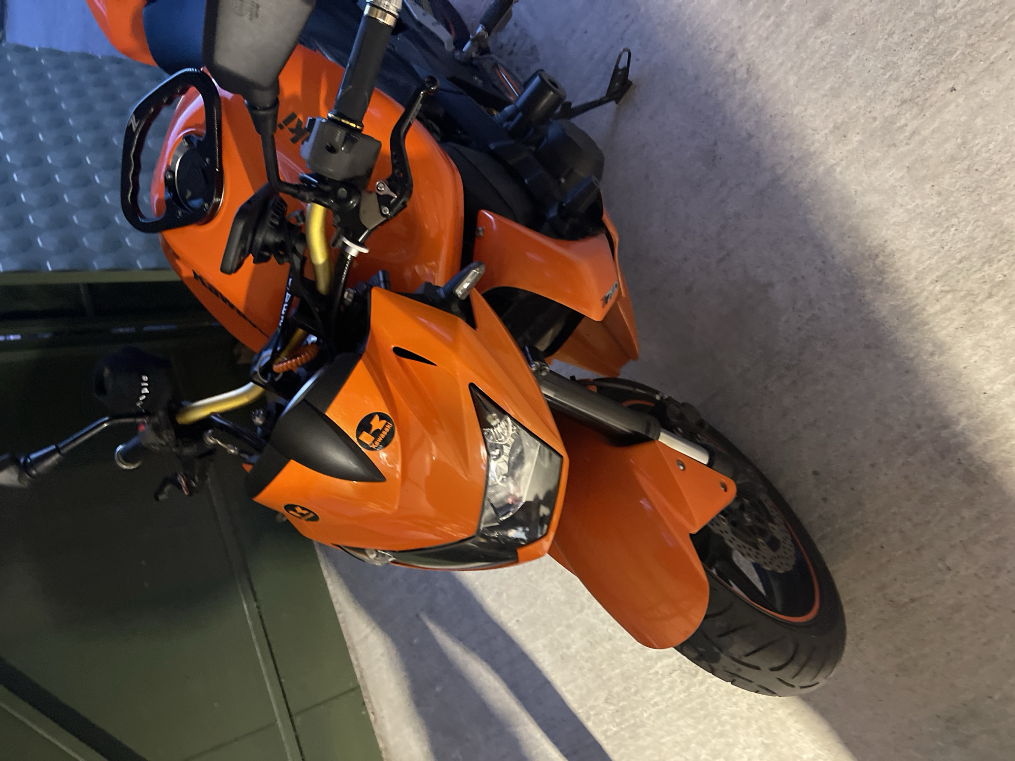 The image shows an orange Kawasaki Z750 motorcycle. The motorcycle is parked indoors, possibly in a garage. The motorcycle is the only subject in the image. There are no people present in the image. The location in the city of Sofia, Bulgaria cannot be determined from the image.