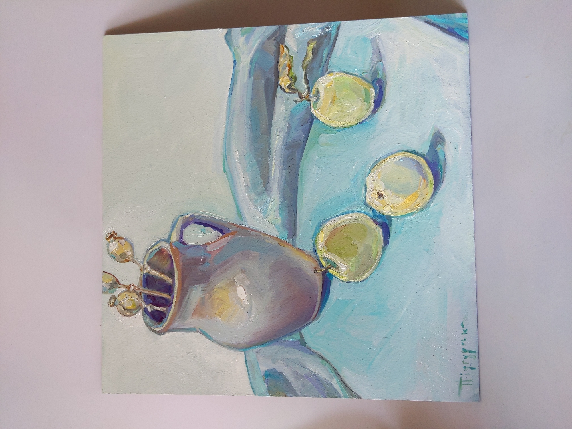 This is an oil painting of a still life. The painting depicts a ceramic jug with dried poppy seed heads in it, placed on a light blue surface. Three light green apples are arranged in front of the jug, with one apple to the left, one in the center, and one to the right. A blue fabric is draped behind the jug. The painting is signed in the lower left corner with Cyrillic script. The image is a photograph of the painting, taken against a plain background, with the painting itself oriented landscape. There is no information in the image to indicate its location in the city of Rivne, Ukraine.