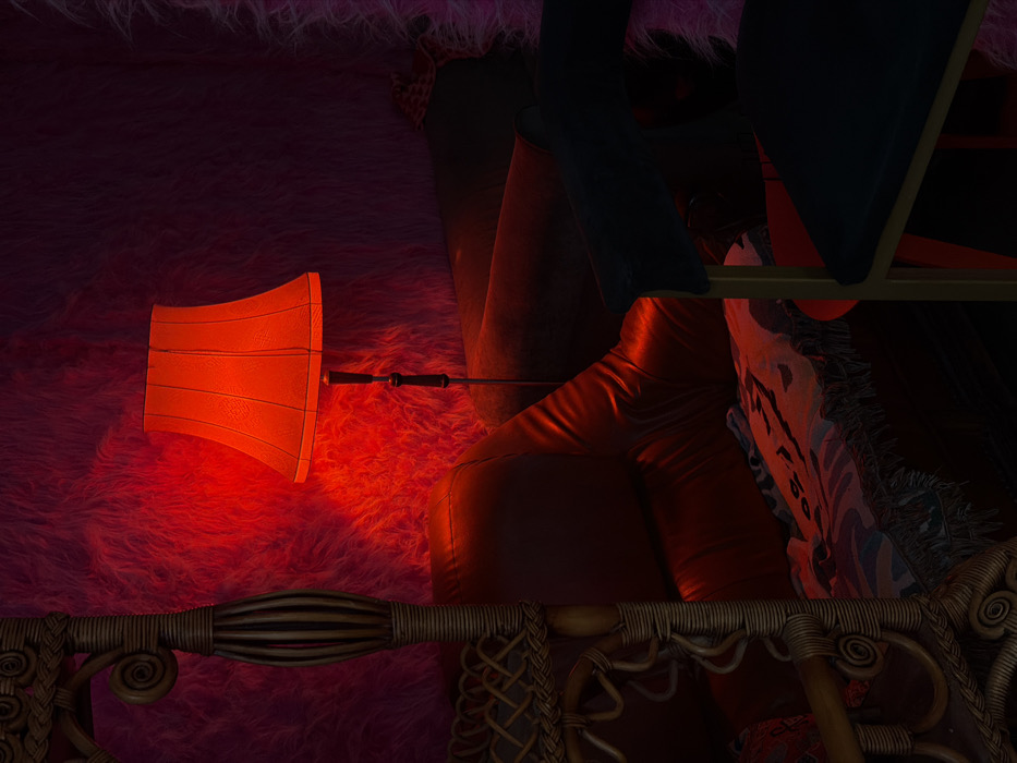 An interior scene is illuminated by a prominent red light source, casting a crimson glow across the environment. The walls are textured with a deep fuchsia, shaggy material. A tall floor lamp with a conical red fabric shade stands centrally, emanating the primary red light. To the left, a substantial piece of light-colored wicker furniture, featuring ornate woven patterns and spiral details, is partially visible, suggesting a bed frame or decorative screen. Below the lamp and adjacent to the wicker structure, a dark red leather sofa or couch is present, draped with a patterned, fringed throw blanket displaying animalistic motifs. In the lower right foreground, a segment of a modern chair with dark upholstery and a light-colored metallic frame is visible, partially obscuring a small, round, dark red table behind it. No individuals or specific actions are depicted. The image lacks identifying markers to pinpoint its location within Moscow, Russia.