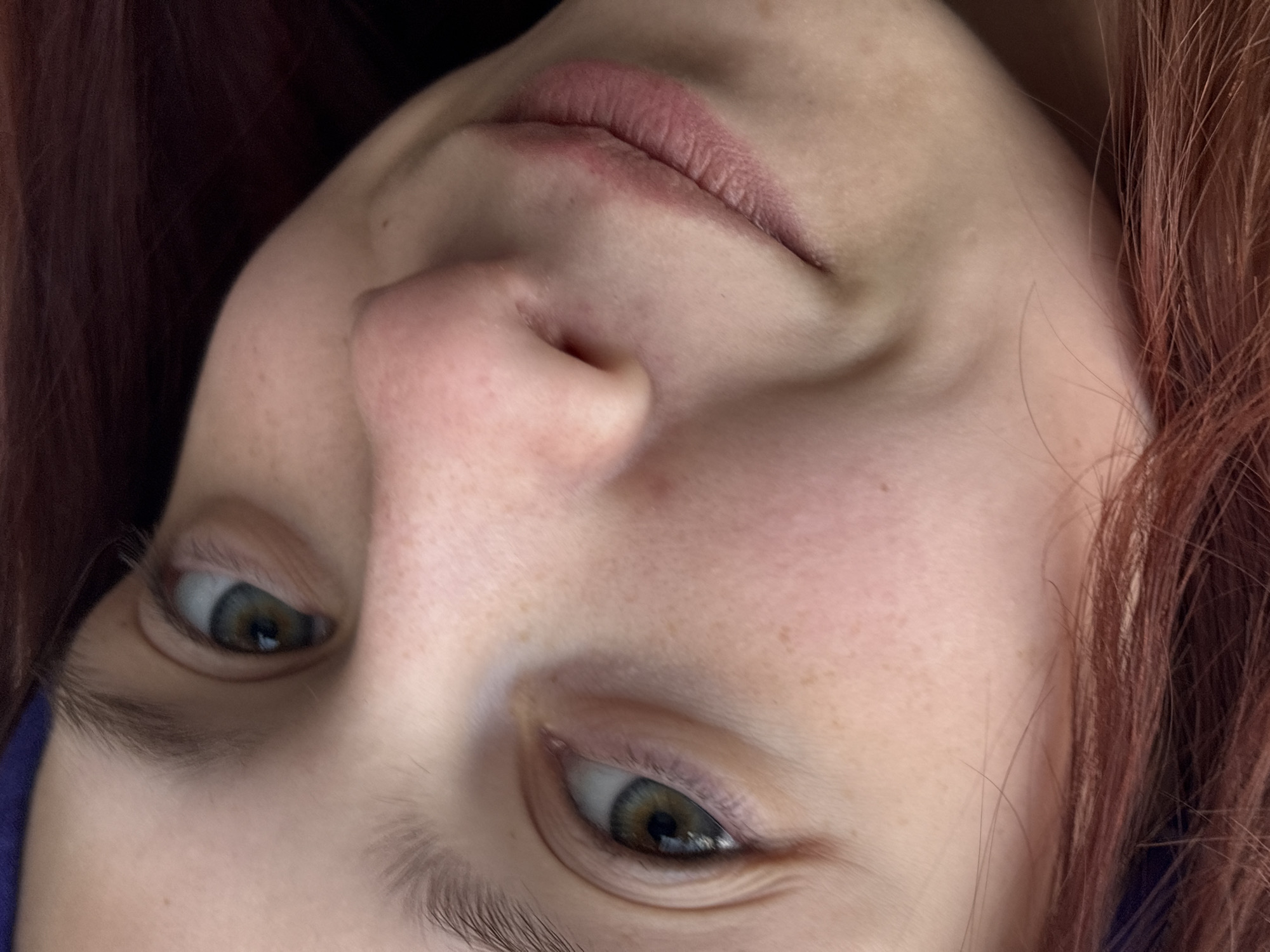 A close-up of a person's face, viewed from a low angle. The person has fair skin with freckles, reddish-brown hair, and eyes that appear to be a mix of green and brown. The focus is on the nose, lips, and eyes. The background is blurry. There is no evidence to suggest this picture was taken in Perm, Russia.