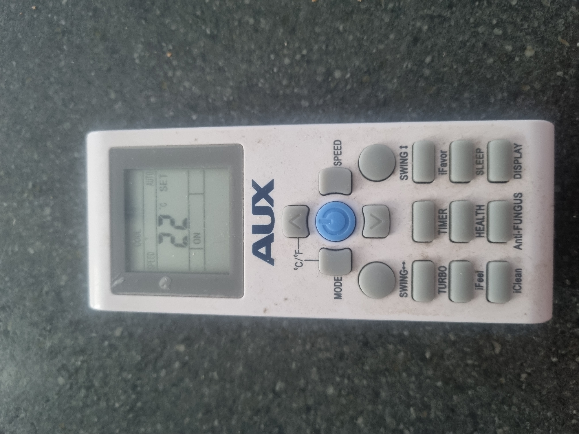 A white remote control with a black digital display rests on a dark, speckled surface, likely a countertop. The remote has various buttons for an air conditioner, including "MODE," "SPEED," "SWING," "TURBO," "TIMER," "iFeel," "iClean," "HEALTH," "Anti-FUNGUS," "DISPLAY," "AUTO," and "SLEEP." The display shows "22" degrees Celsius, set to "COOL" mode and "ON." The remote is slightly dirty. The background is out of focus, showing a textured, dark surface. There is no visible indication of location in Samara, Russia.